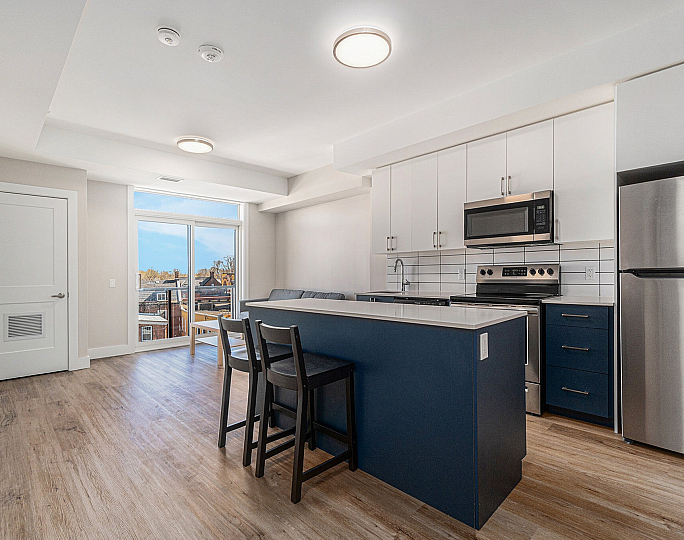 Modern open-concept kitchen and living area with sleek cabinetry, stainless steel appliances, and large windows offering a bright city view.