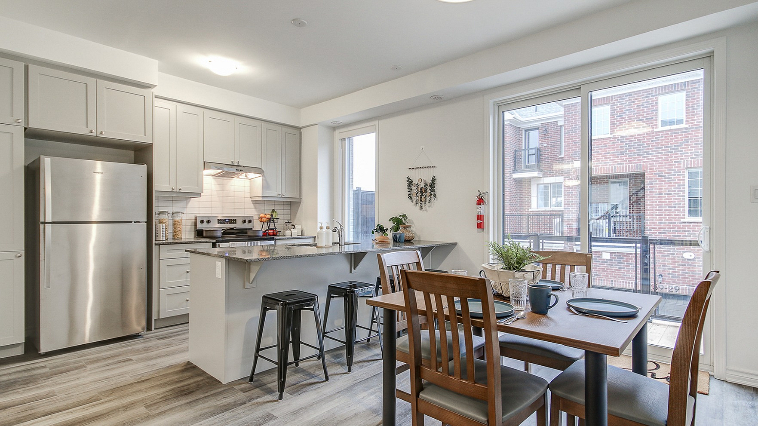 Modern open-concept kitchen and dining area with stainless steel appliances, elegant light grey cabinetry, and stylish wood flooring.
