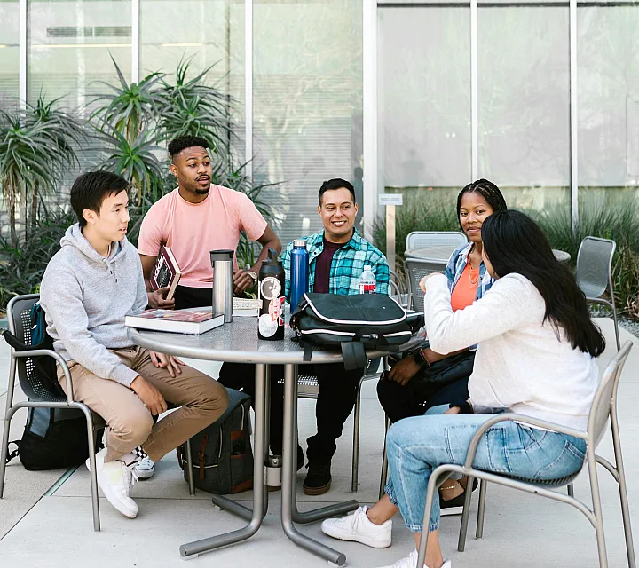 Vibrant outdoor study session with a diverse group of students gathered around a table, enjoying a modern courtyard setting.