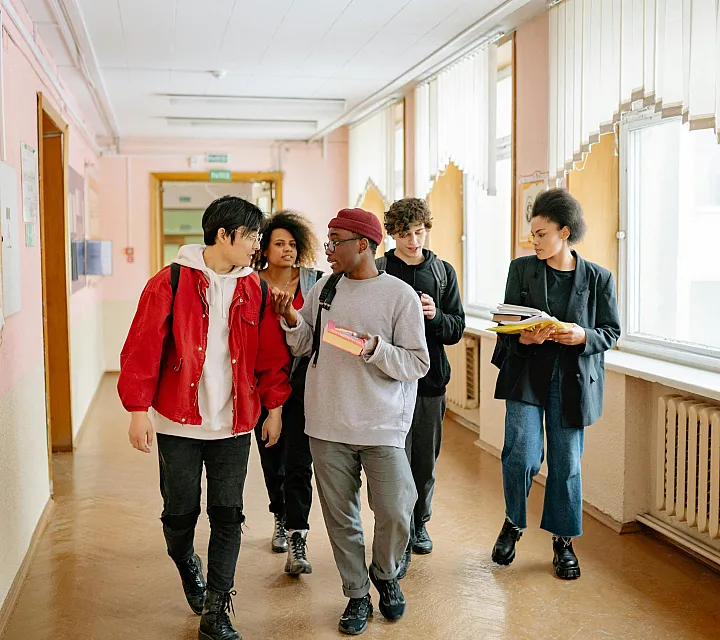 Vibrant group of students walking through a bright school hallway, carrying books and engaging in lively conversation.
