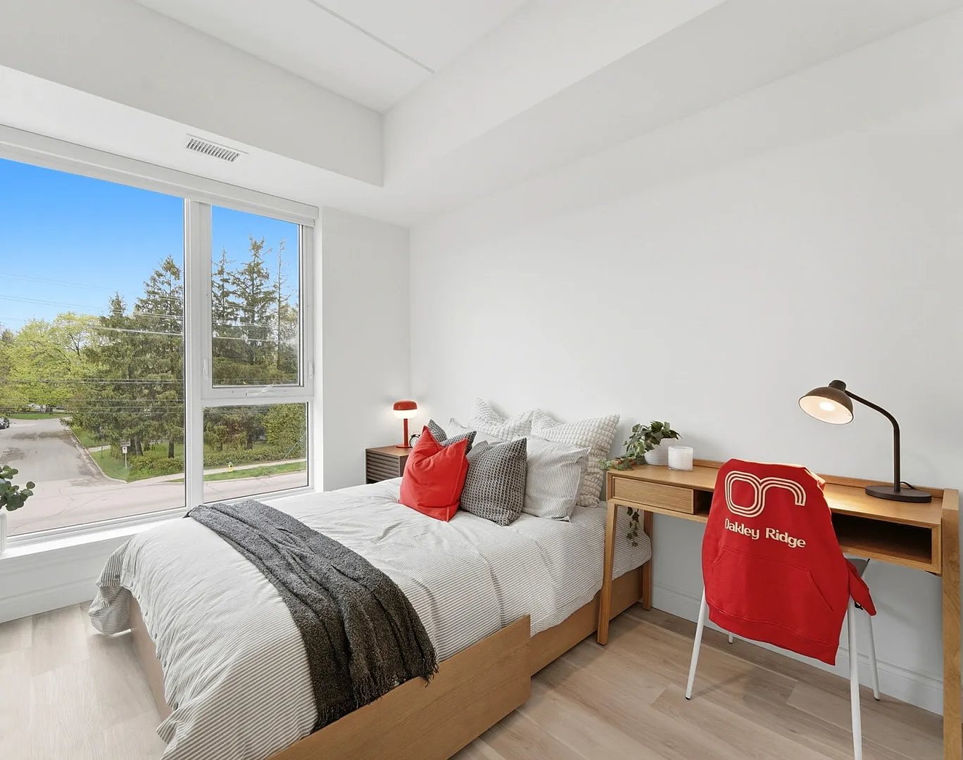 Inviting bedroom filled with natural light, featuring a cozy bed, modern desk, and scenic view from a large window.