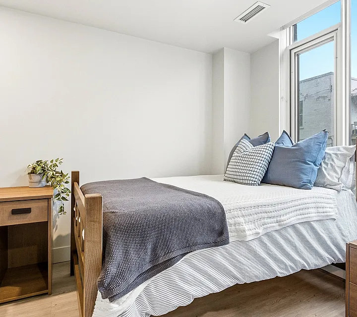 Bright and cozy bedroom featuring a stylish wooden bed with plush pillows, a sleek desk, and a large window with a charming urban view.