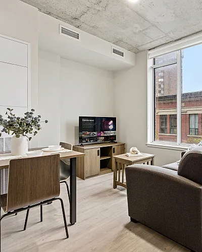 Modern living space featuring a cozy seating area with a plush sofa, a stylish dining table, bright windows with an urban view, and contemporary decor.