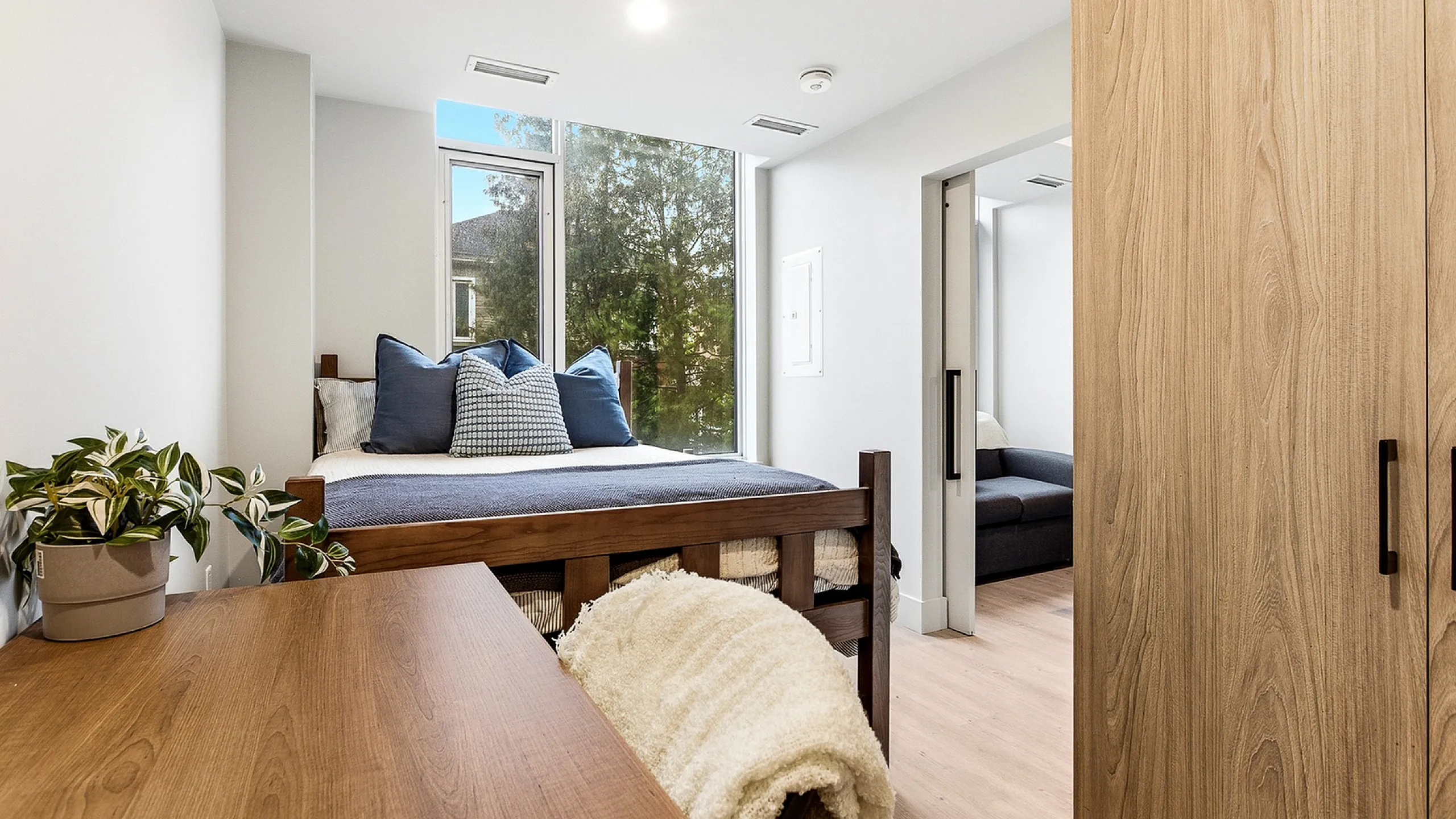 Bright and inviting bedroom with a modern wood desk, cozy bed, and large window offering serene views.