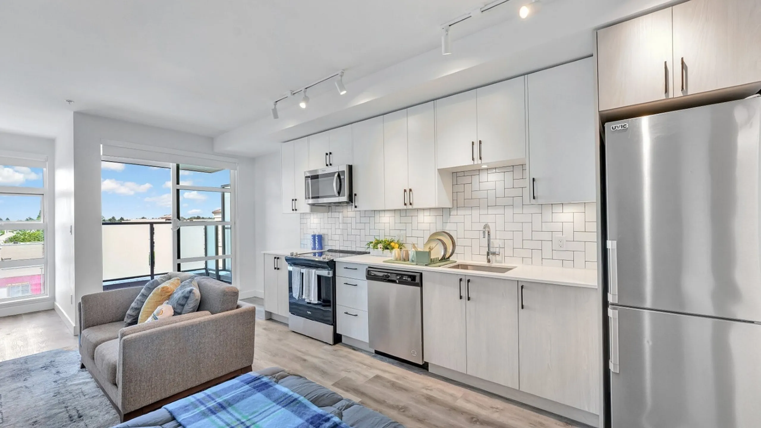 Bright, modern apartment kitchen with stainless steel appliances, sleek cabinetry, and cozy living area with large windows offering a picturesque view.