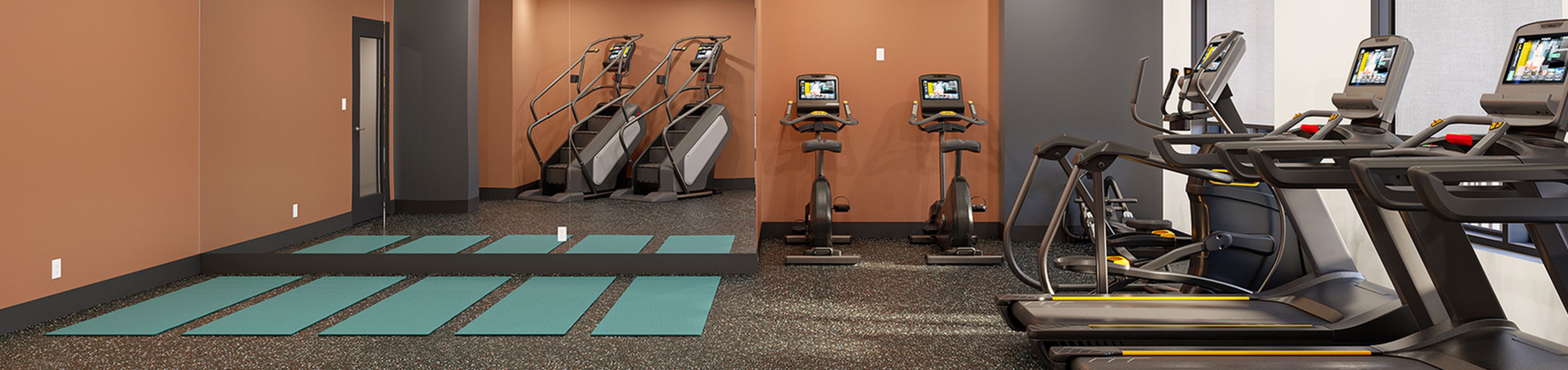 Modern fitness center featuring state-of-the-art treadmills, exercise bikes, stair climbers, and yoga mats in a spacious, well-lit room.