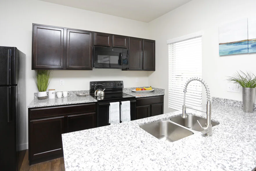 Modern kitchen with dark wood cabinets, black appliances, and granite countertops at City Garden in Ogden.
