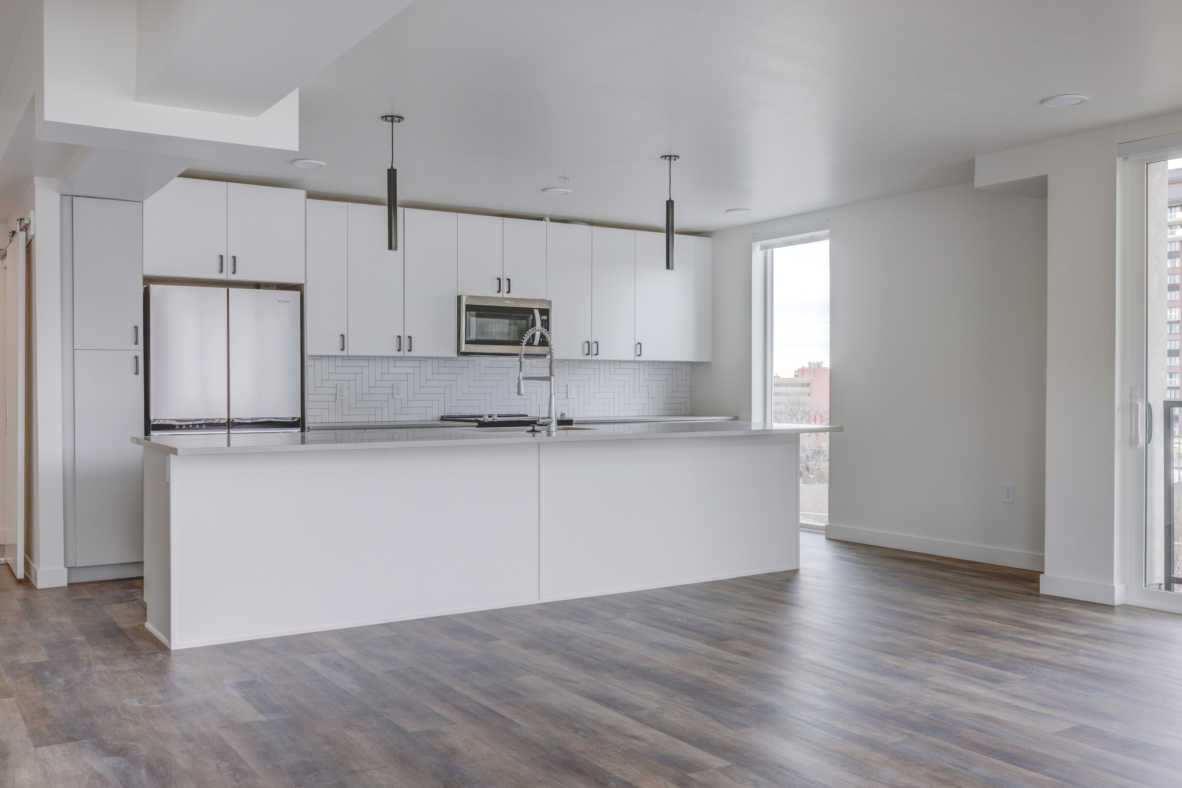 Modern apartment interior at 6th & Main Apartments in Salt Lake City featuring an open-concept kitchen, quartz countertops, stainless steel appliances, and large windows.