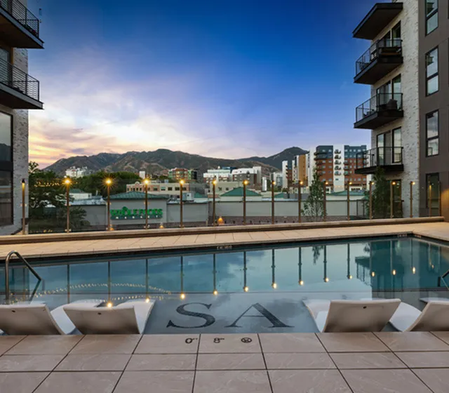 Sunset view of Sugar Alley's pool deck with twinkling lights and mountain backdrop in Sugar House