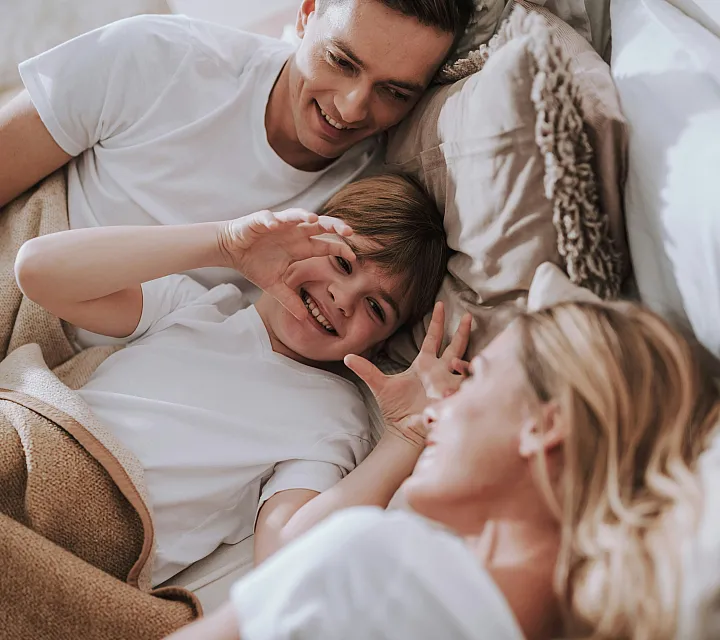 Parents and child relaxing and smiling together in bed on a cozy morning