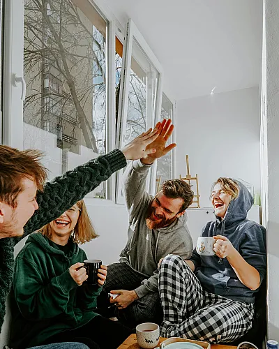 Group of friends sitting indoors, laughing and high-fiving over coffee and tea