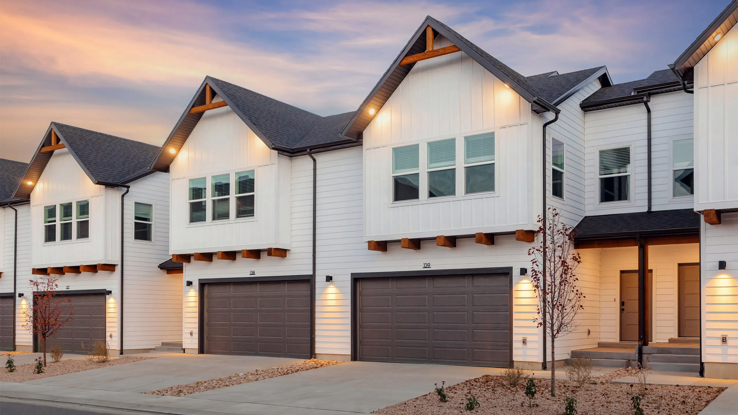 Bright white Railrunner Townhomes with black roofs, attached garages, and clean landscaping in Roy, Utah