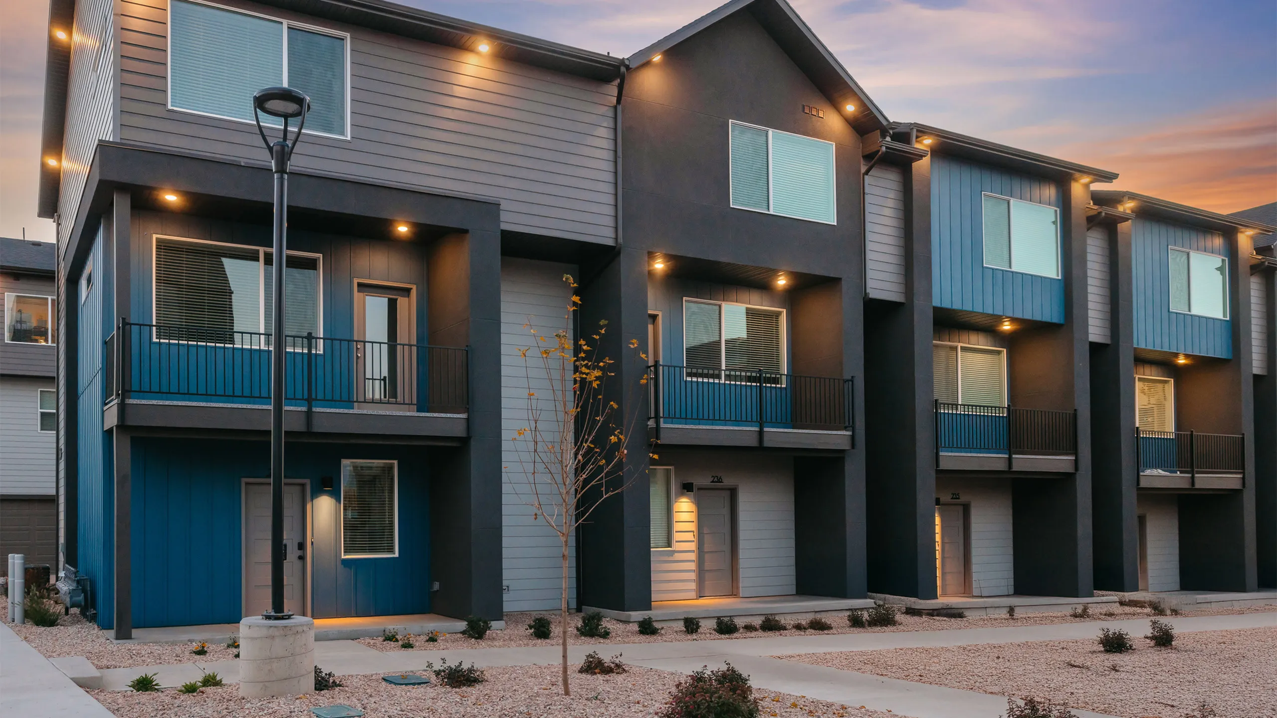 Row of Blue Railrunner Townhomes with garages and young landscaping along the street in Roy, Utah