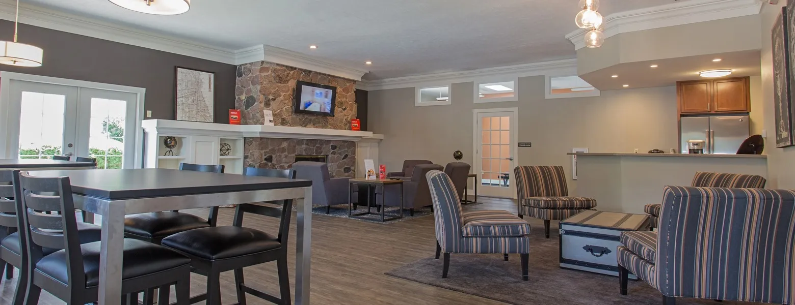 Clubhouse with a large stone fireplace with a TV mounted above it. Several seating areas within the room. A large community kitchen is to the right.