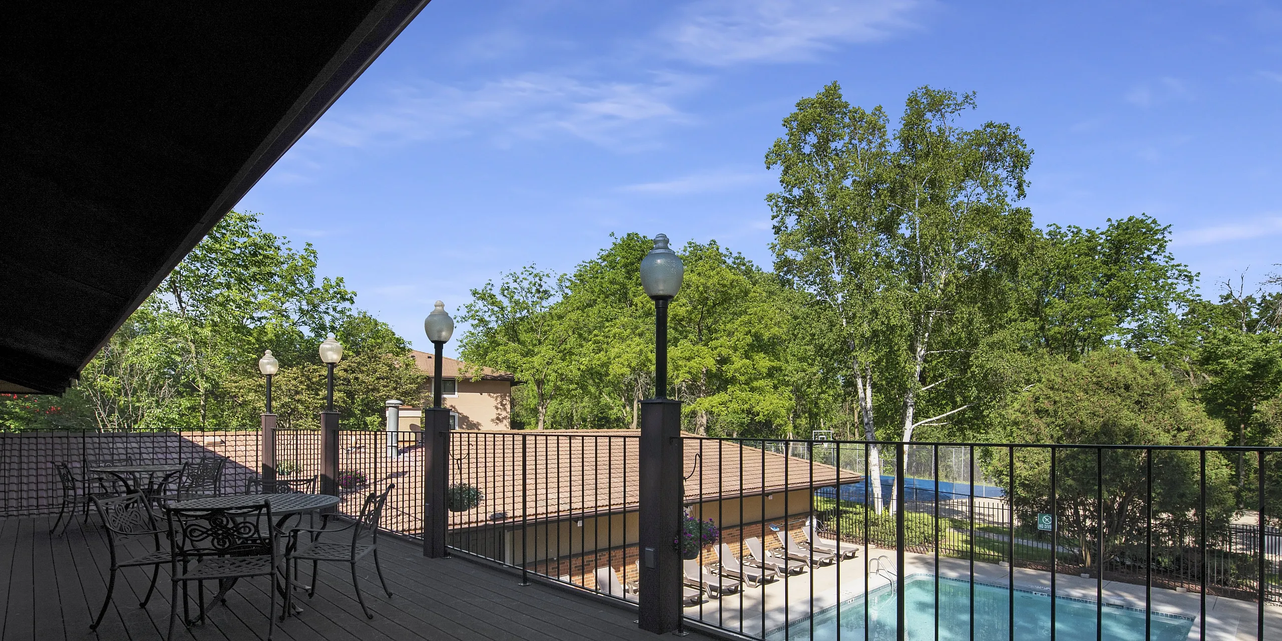 Spacious community balcony overlooking a serene outdoor pool with elegant seating and lush green trees.