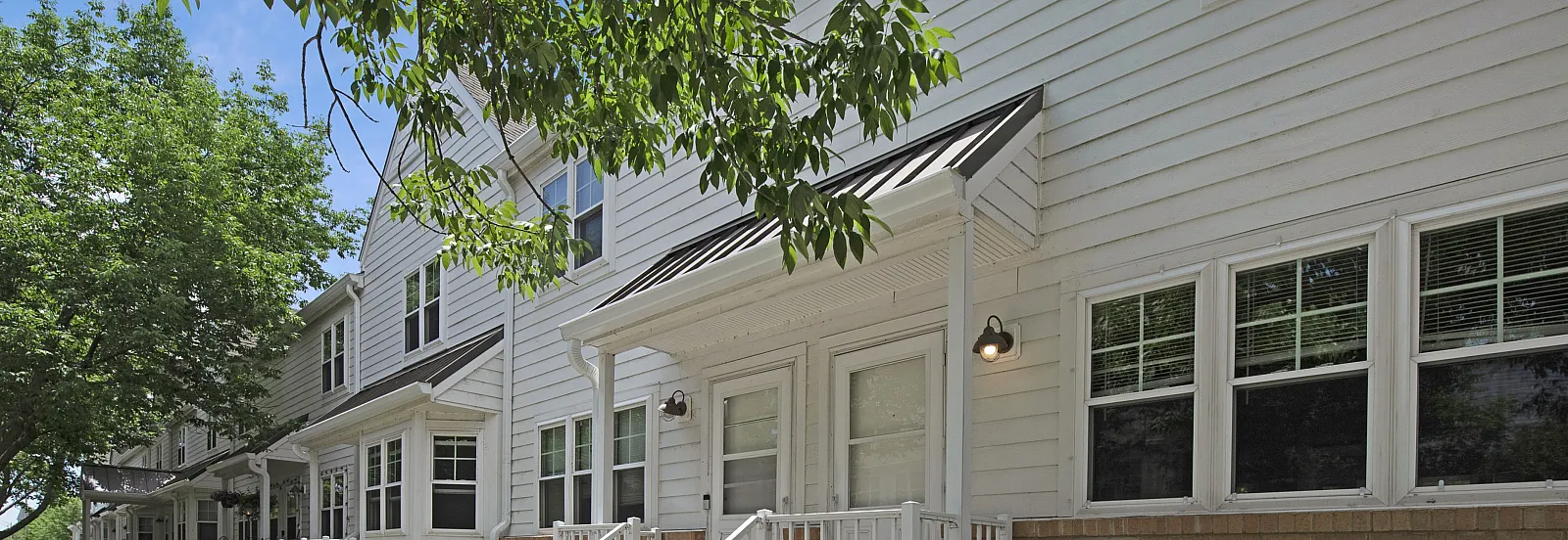 Charming townhouse row with lush greenery, white siding, and inviting porches.