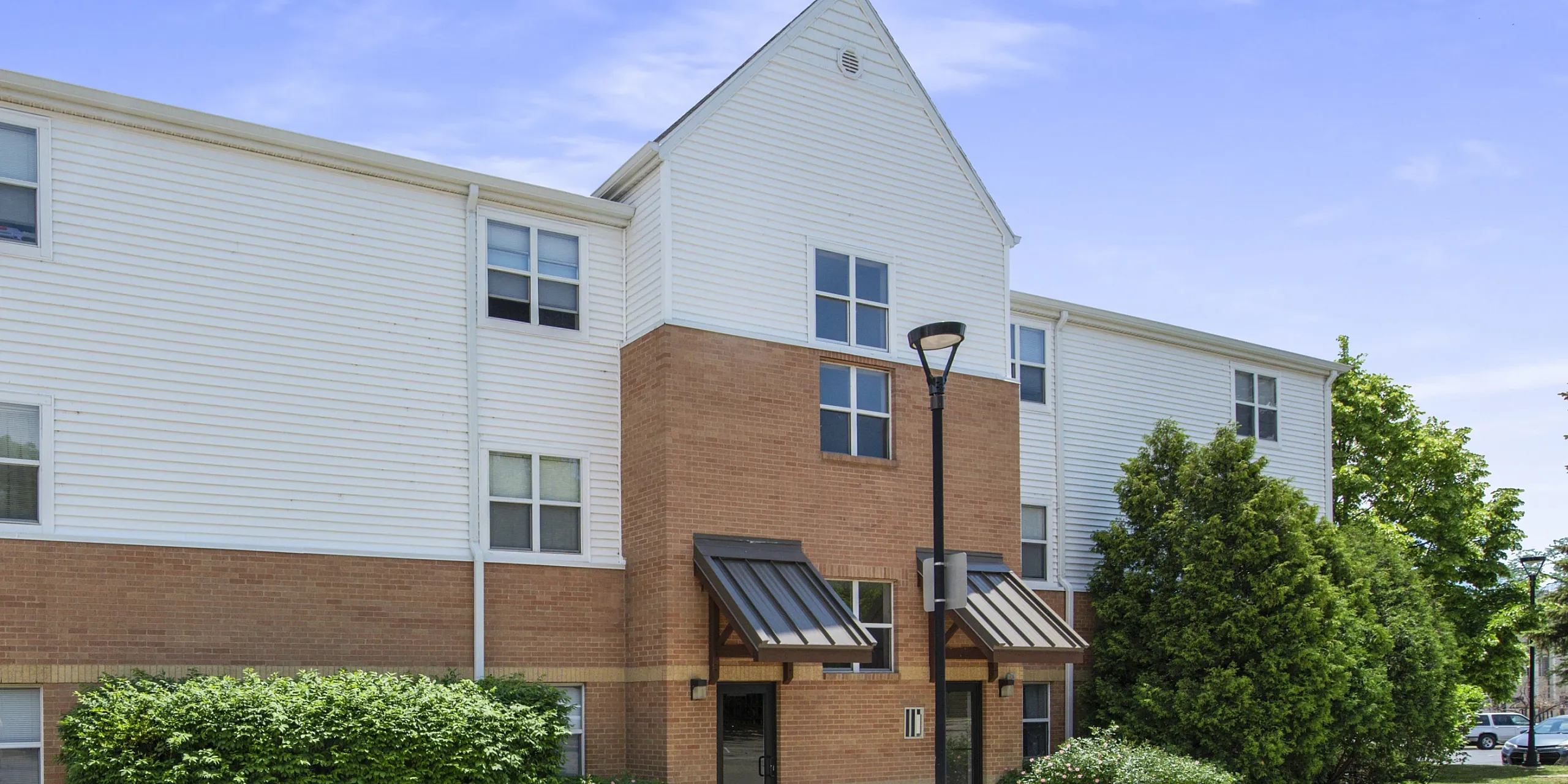 Modern apartment building with brick and siding, surrounded by lush greenery on a sunny day.