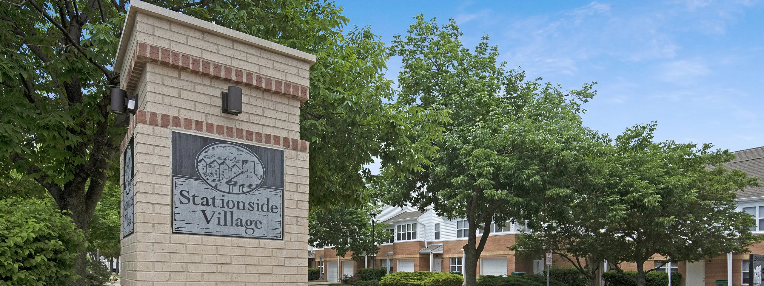 Entrance of Stationside Village with signage, lush greenery, and residential buildings