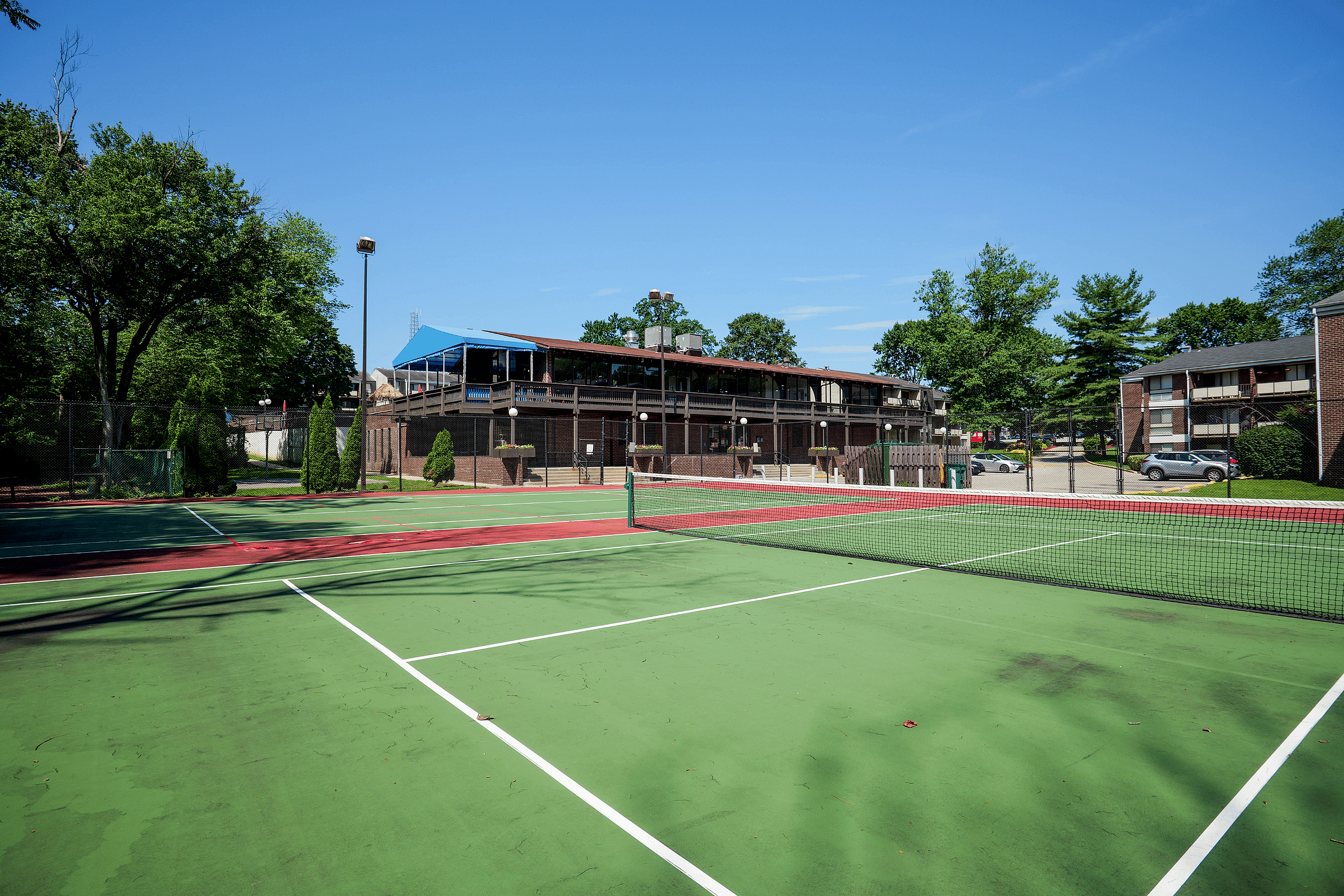 Inviting tennis court with a scenic apartment complex backdrop, surrounded by lush green trees under a clear blue sky.