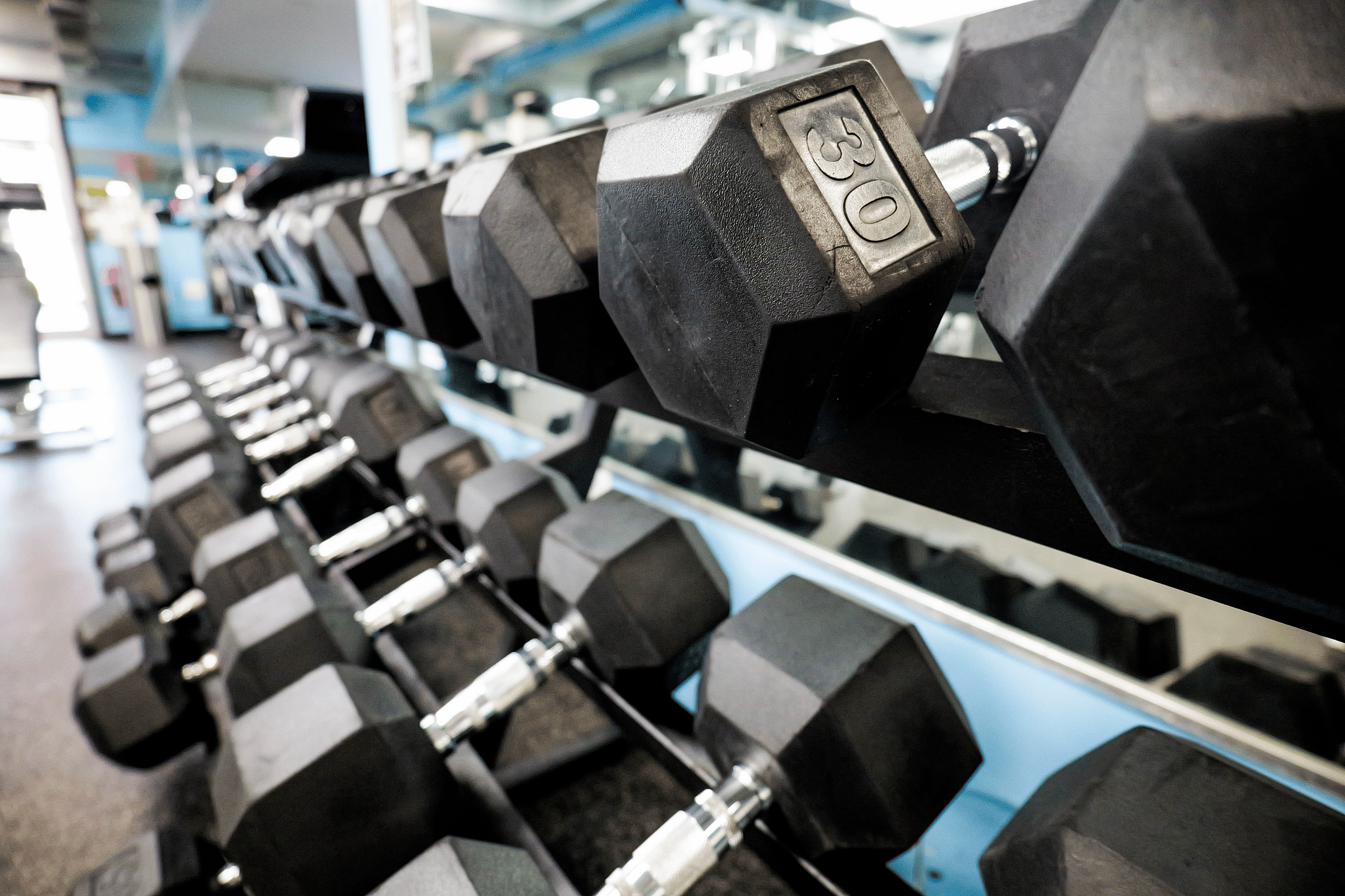 Contemporary gym with a sleek row of black hexagonal dumbbells on a mirrored rack, perfect for fitness enthusiasts.