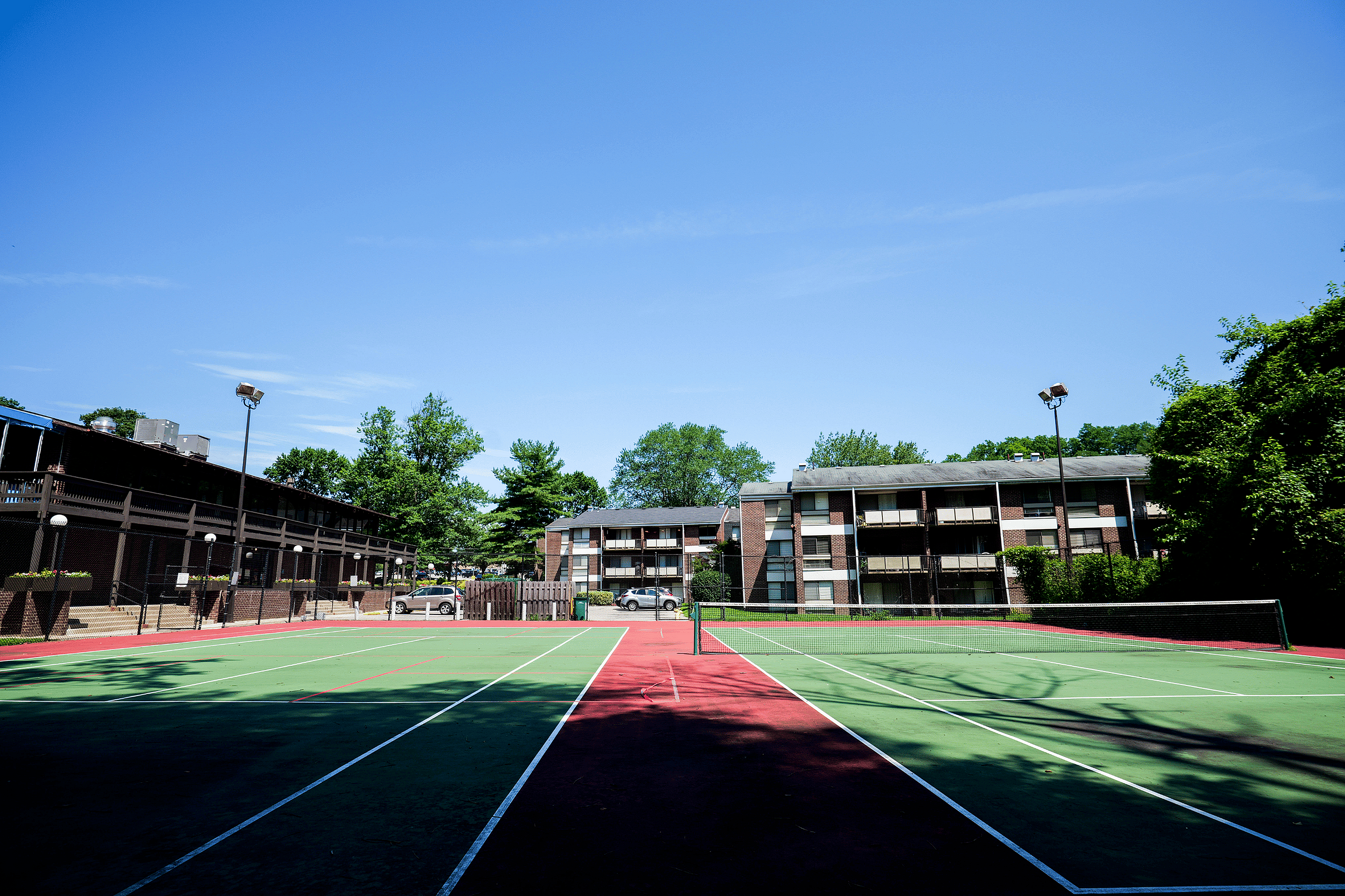 Inviting apartment complex with a vibrant tennis court under a clear blue sky, surrounded by lush greenery and stylish buildings.