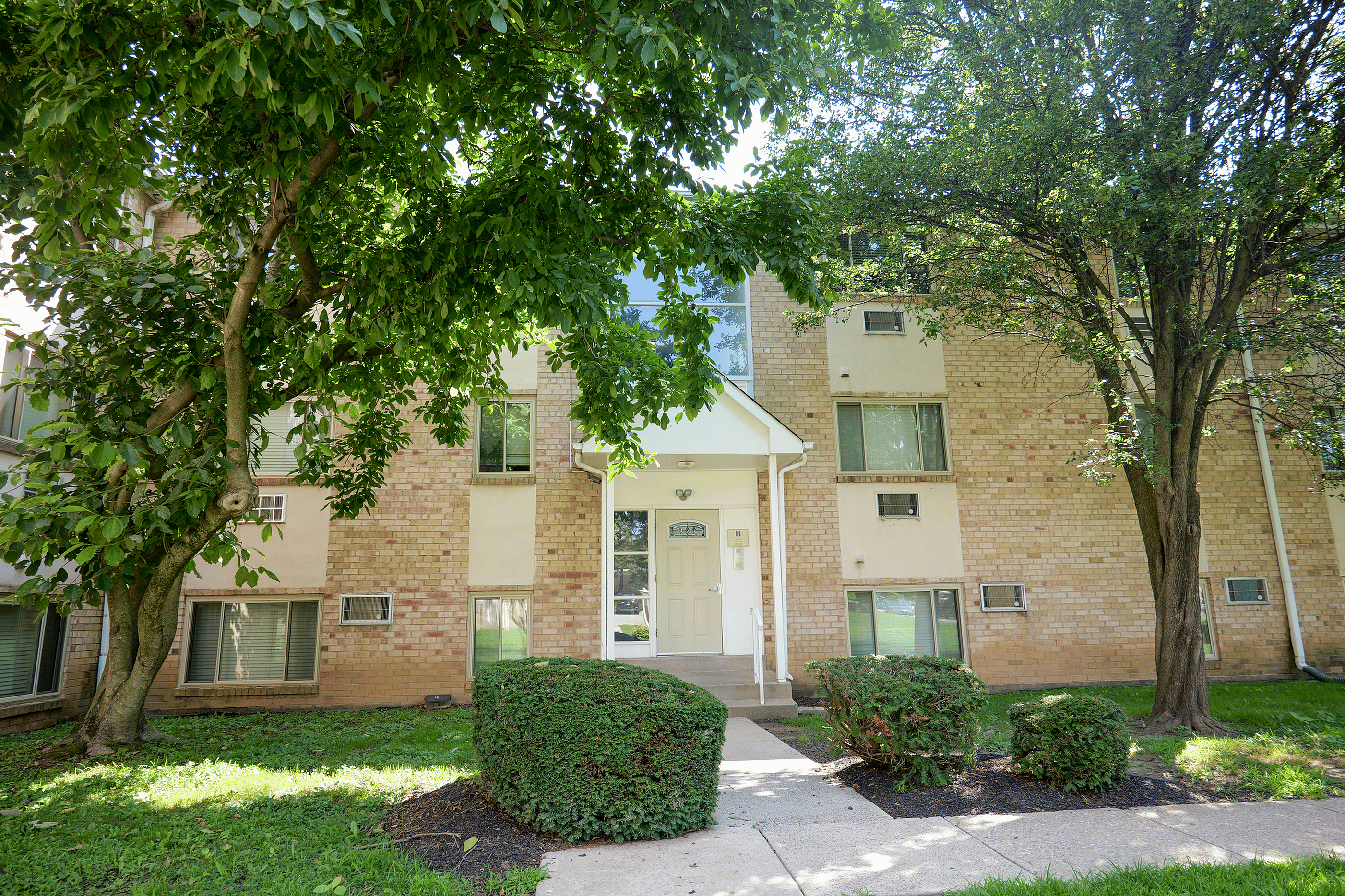 Charming apartment building facade surrounded by lush greenery, featuring a welcoming entrance and well-maintained landscaping.