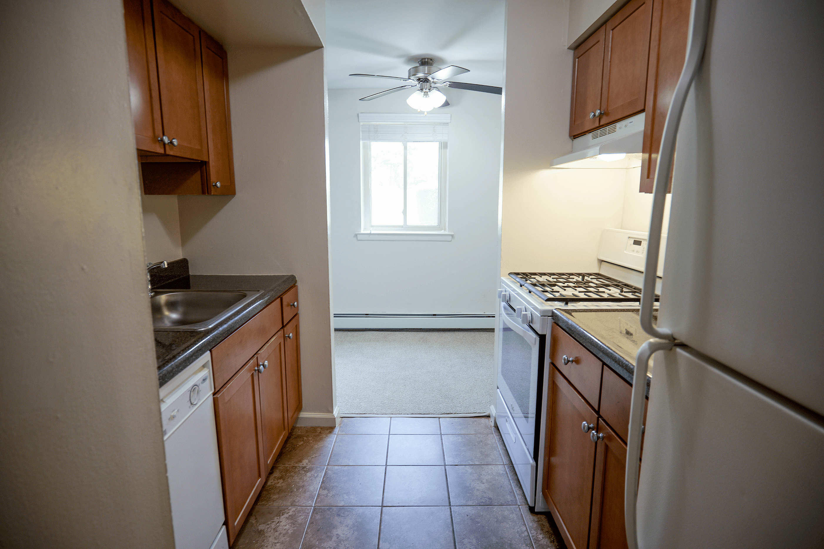 Cozy kitchen with elegant wooden cabinets, sleek countertops, and modern appliances, leading to a bright window-lit area.