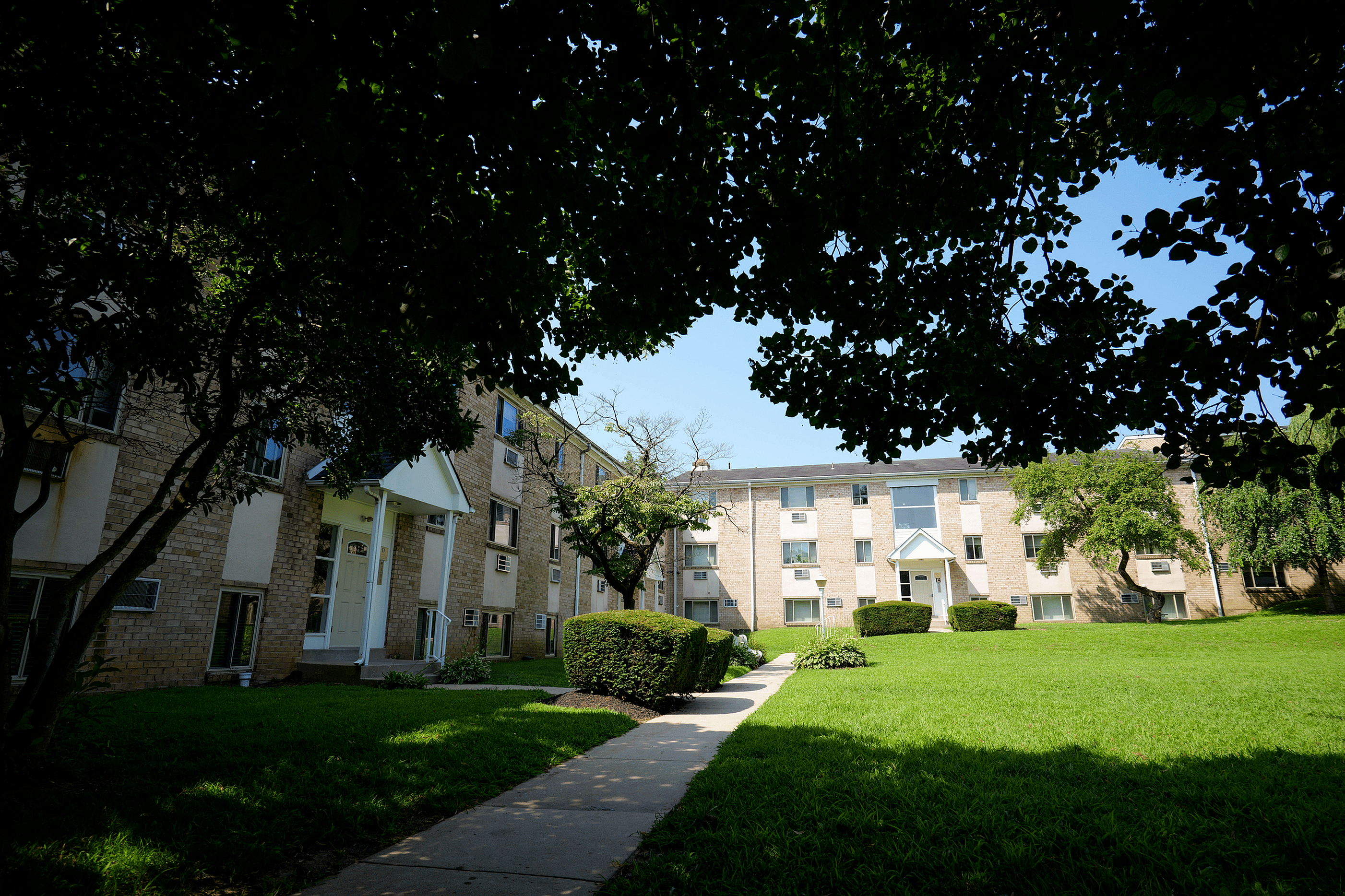 Charming apartment building nestled in lush green surroundings, featuring a peaceful pathway and well-maintained landscaping.