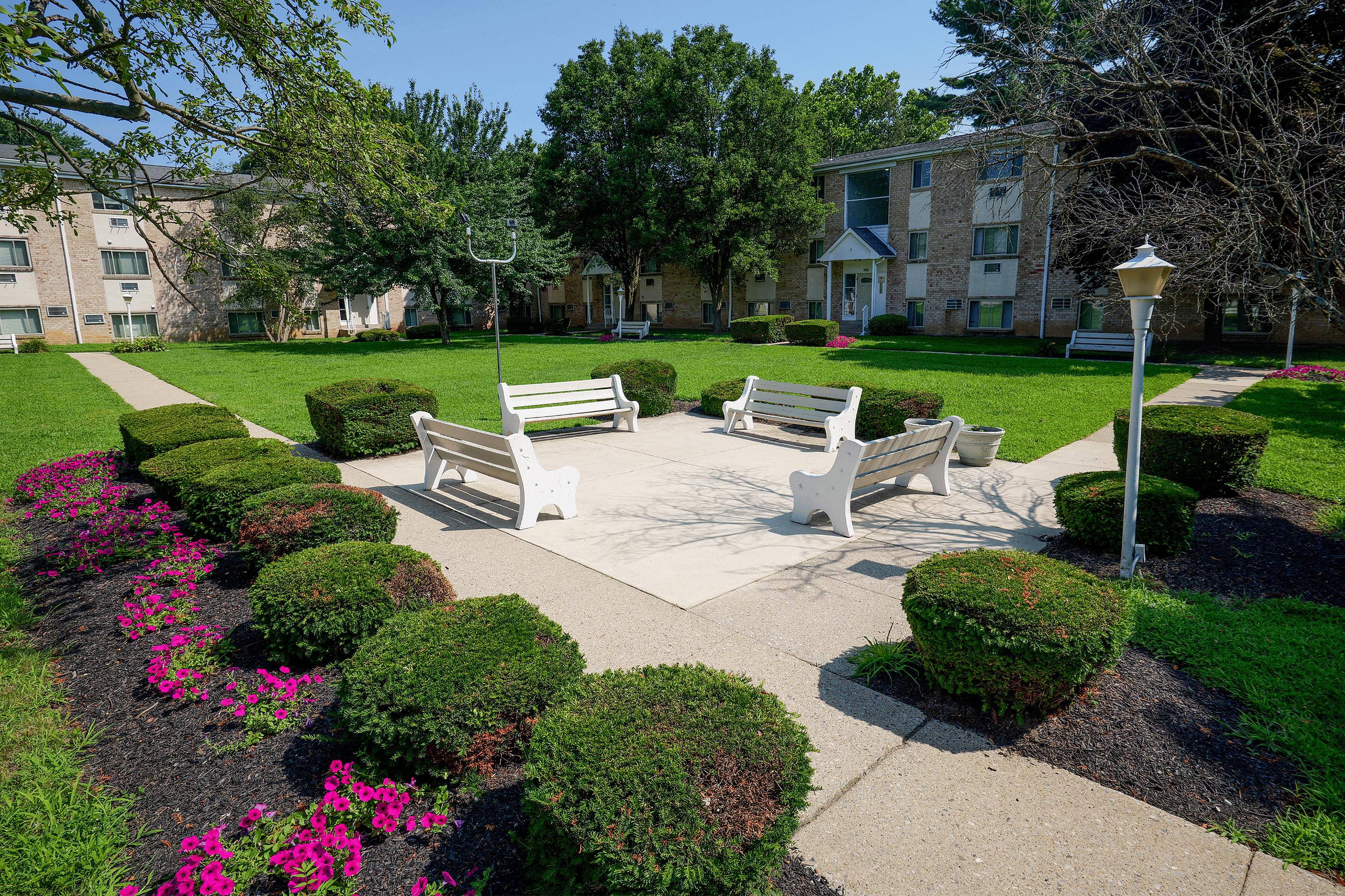 Charming courtyard with benches surrounded by vibrant flowers and manicured bushes, offering a serene community space in a residential complex.