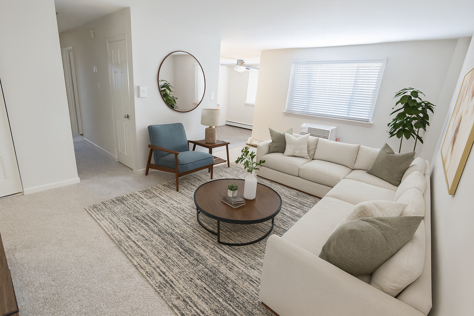 Inviting living room featuring a cozy L-shaped sofa, elegant round coffee table, and chic blue accent chair. Bright, airy space with large window and stylish decor.