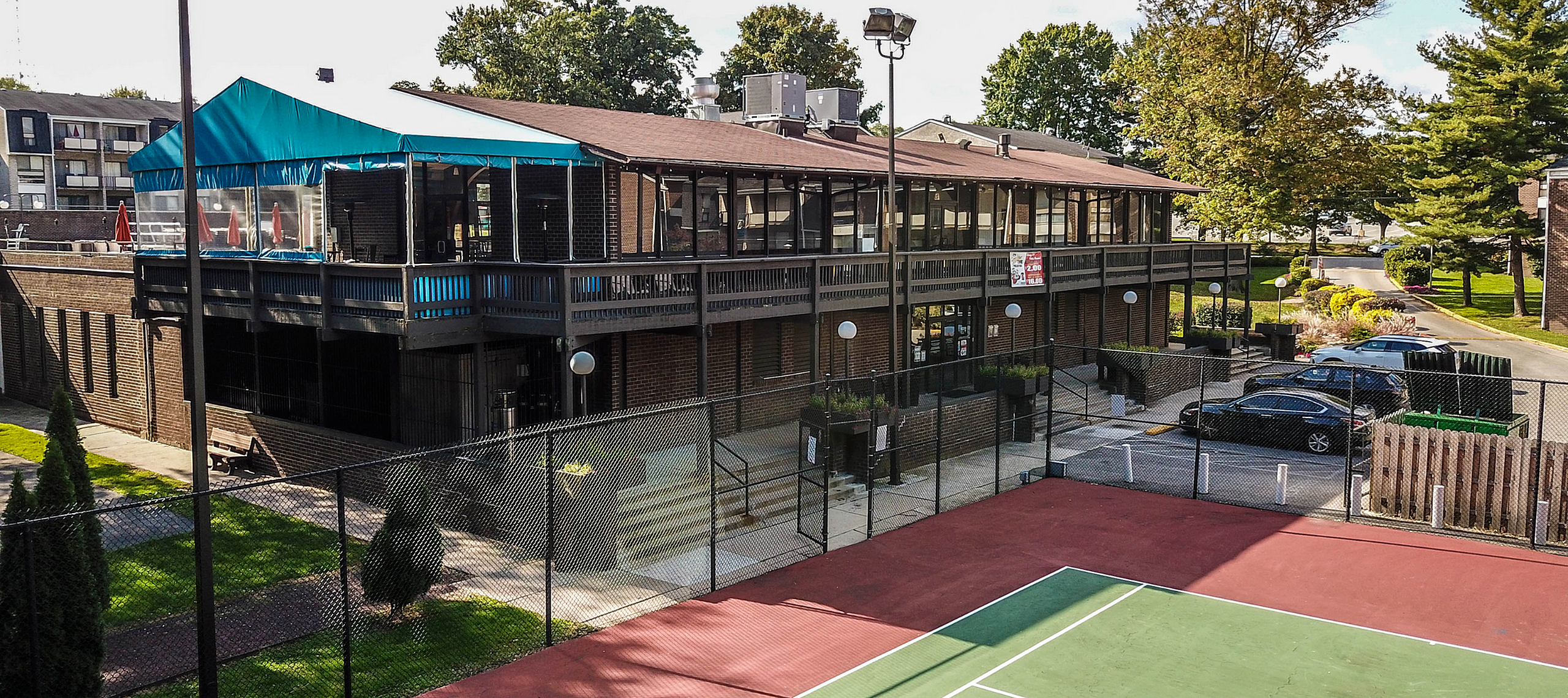 Inviting apartment complex with scenic outdoor tennis court and modern clubhouse, nestled in a lush green setting for an active lifestyle.