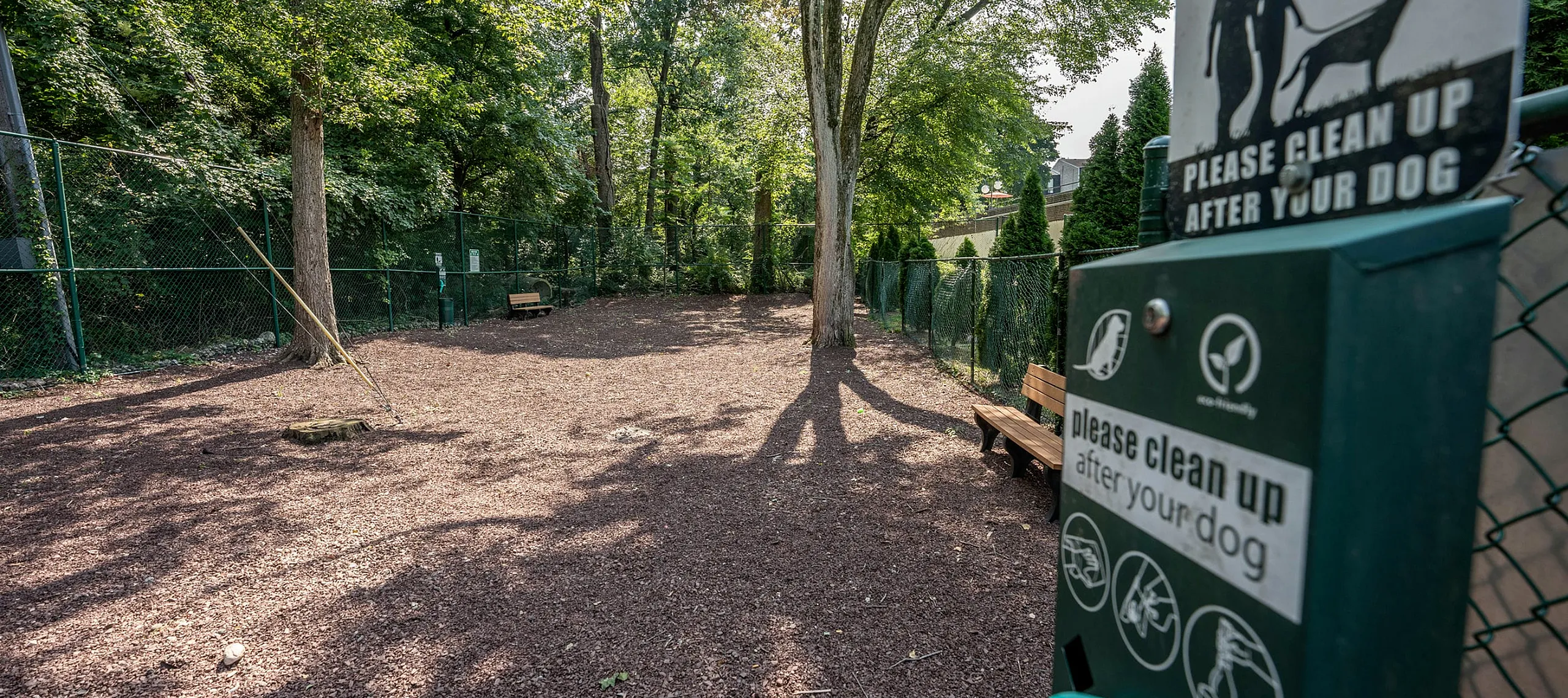 Charming fenced dog park surrounded by lush greenery, featuring wooden benches and eco-friendly waste stations for your pet's enjoyment.
