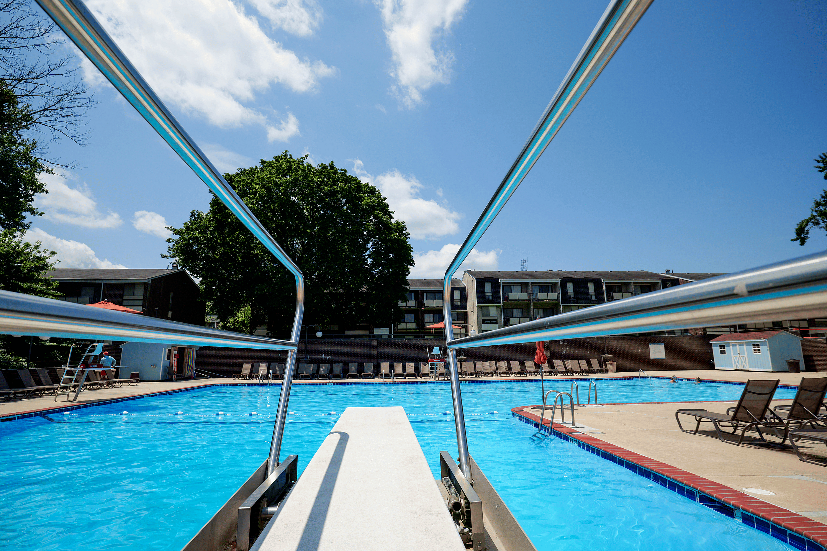 Inviting swimming pool at a modern apartment complex, surrounded by comfortable lounge chairs and lush greenery under a clear blue sky.
