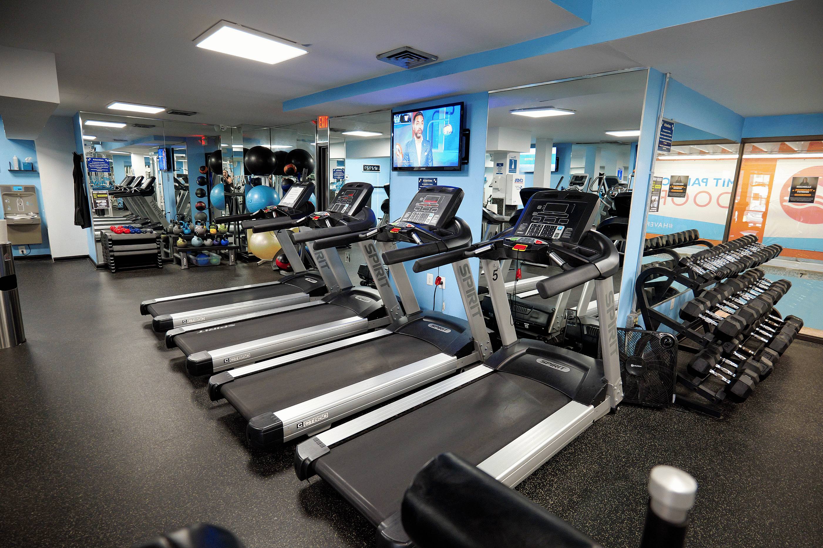 Modern apartment fitness center with state-of-the-art treadmills, free weights, and exercise equipment in a bright, spacious setting.