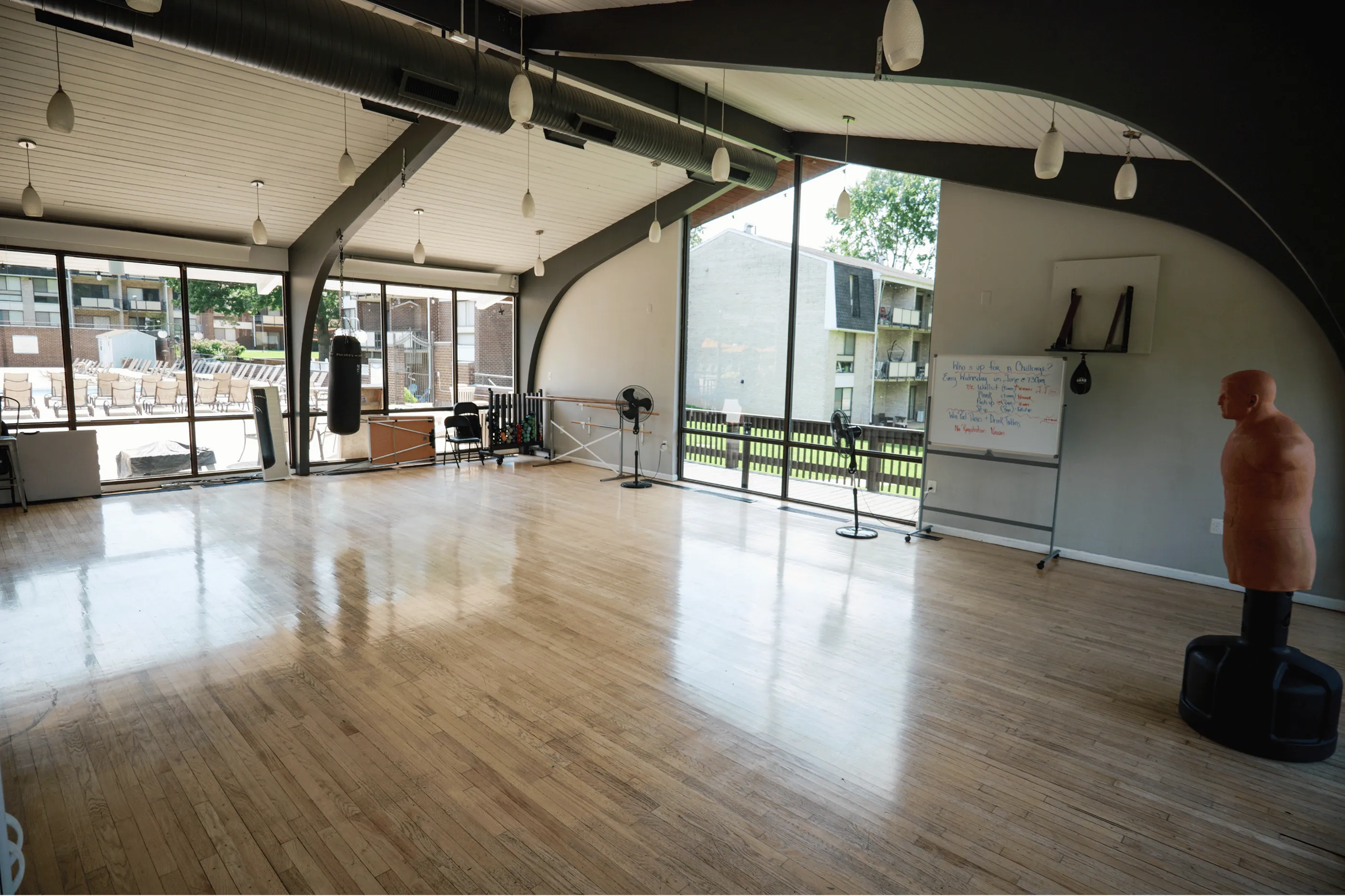Spacious and modern fitness room with large windows offering plenty of natural light, featuring polished hardwood floors and equipped with punching bags, perfect for a well-rounded workout experience.