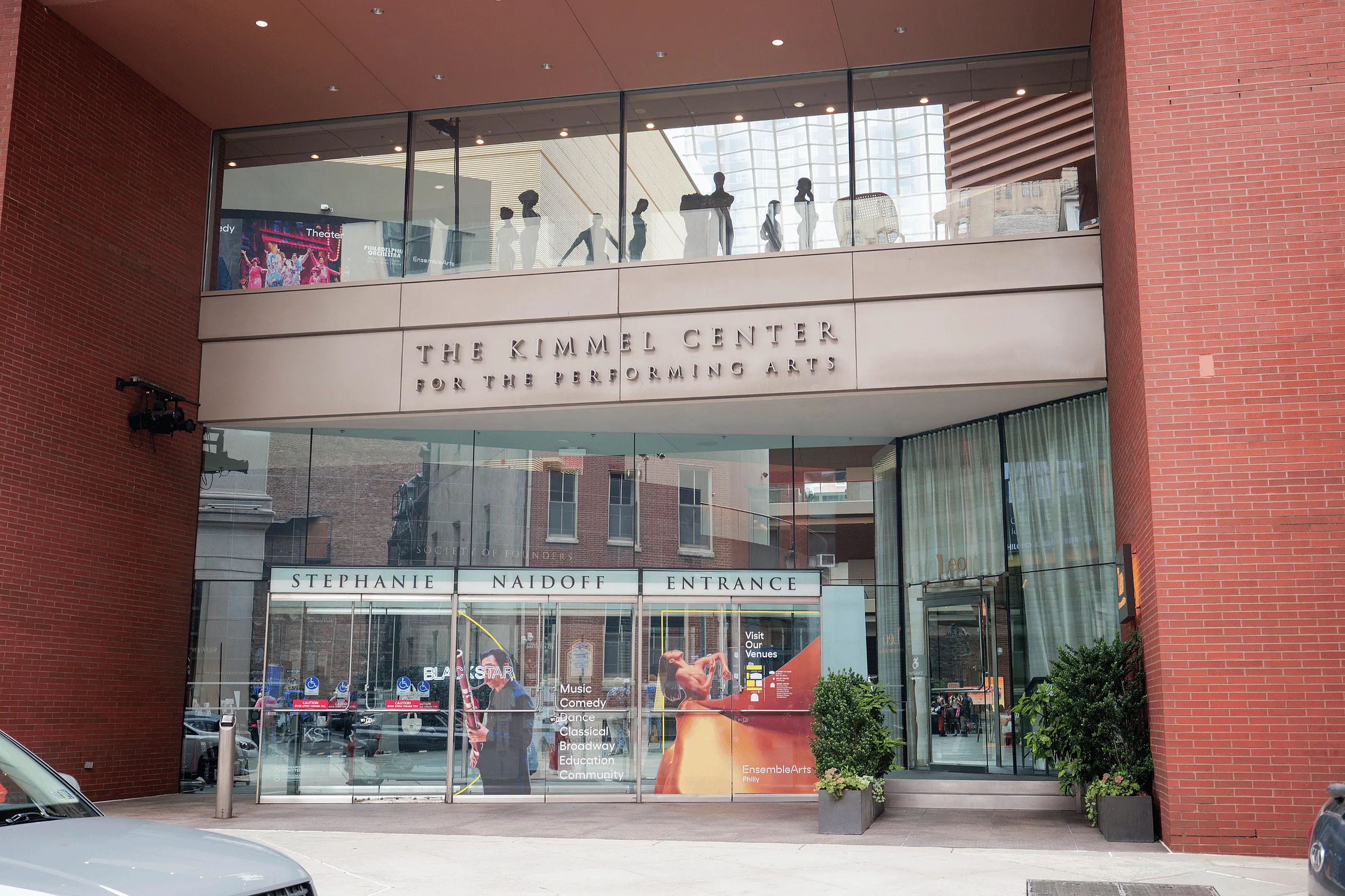 Elegant entrance to a modern performing arts center with large glass windows, contemporary design, and inviting banners advertising music and theater events.