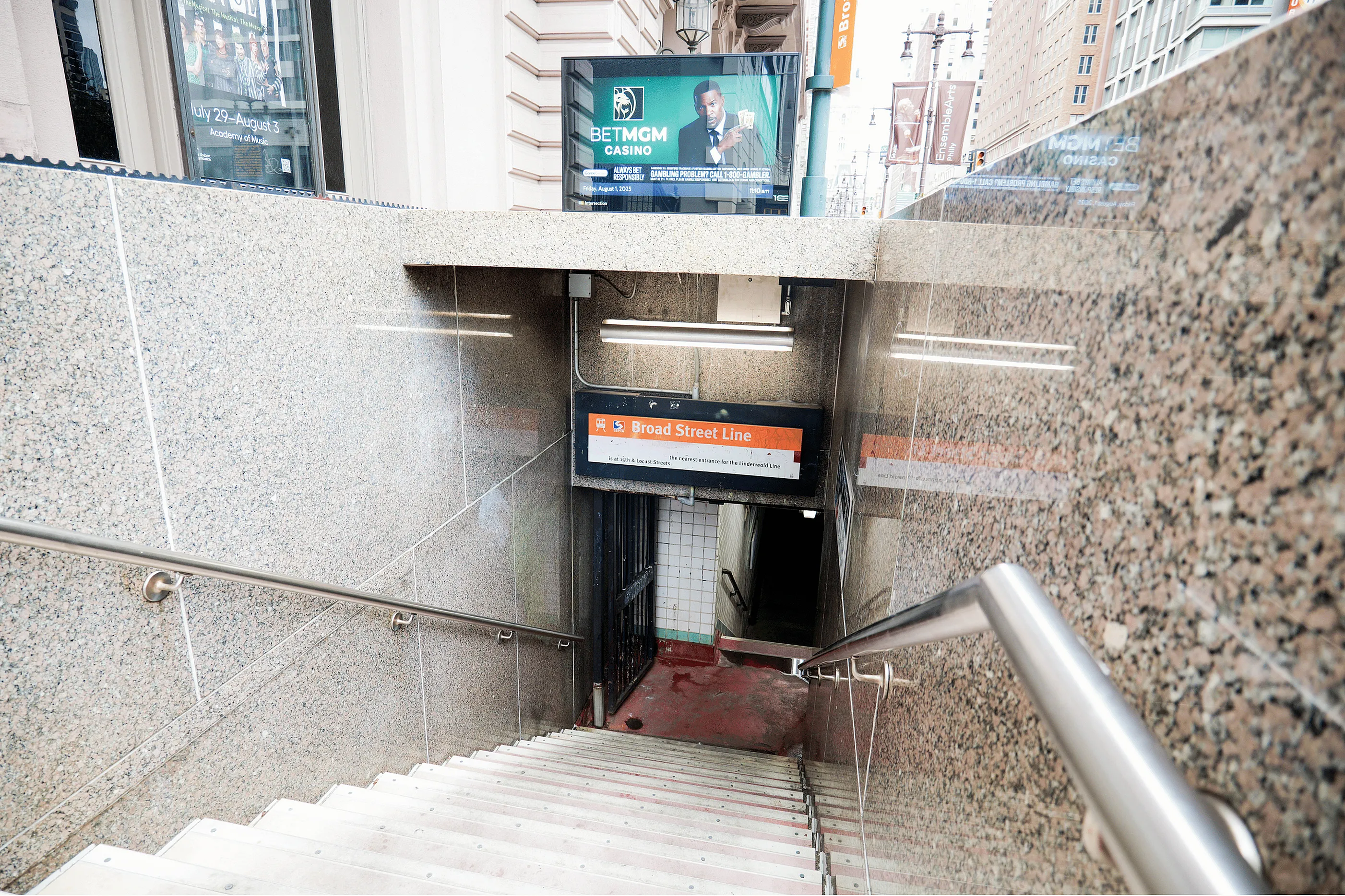 Granite-lined subway entrance for Broad Street Line, featuring modern railings and urban advertisements, offering convenient city access.