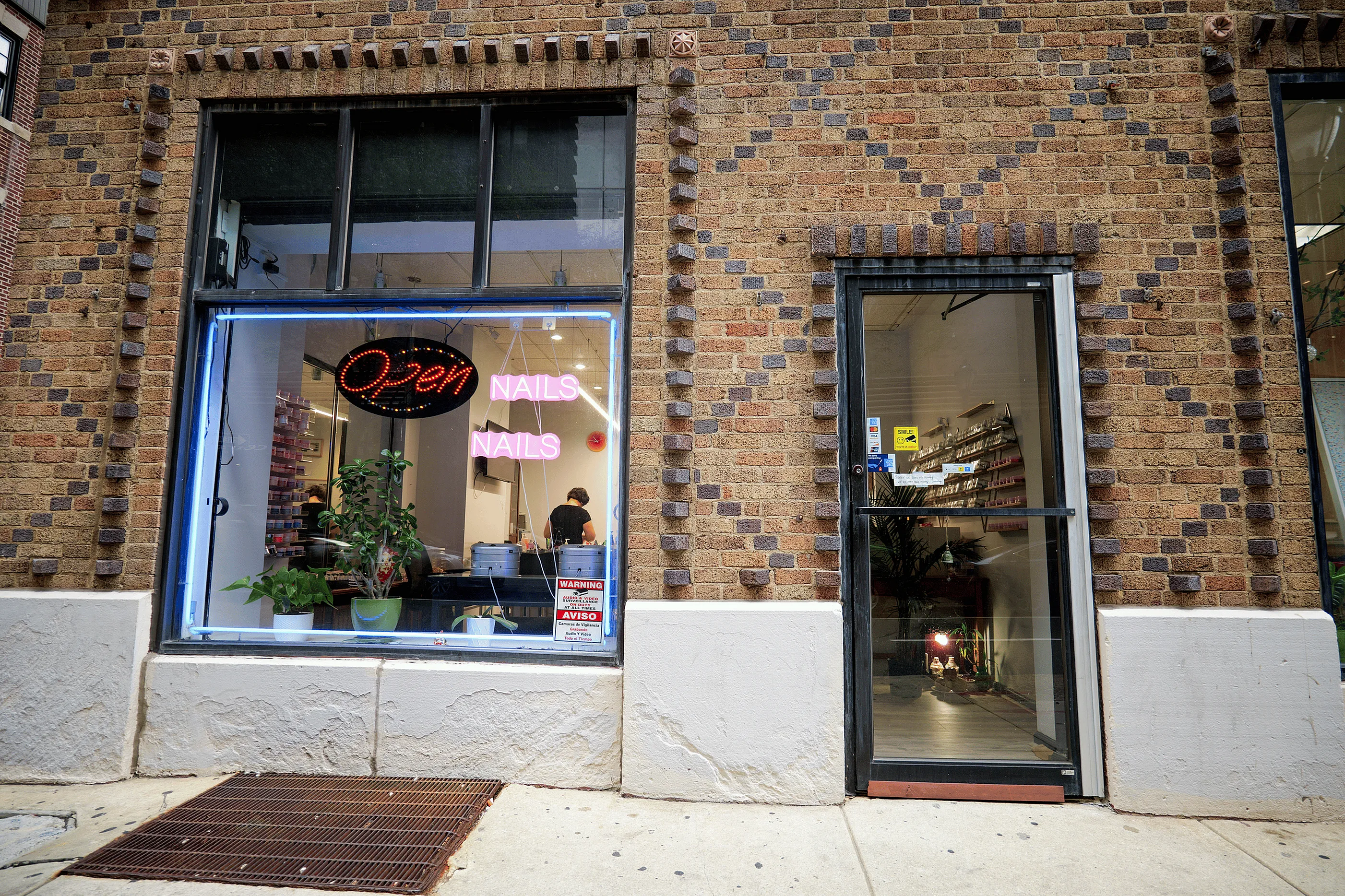 Charming nail salon storefront with neon 'Open' sign, vibrant plants, and inviting brick facade.