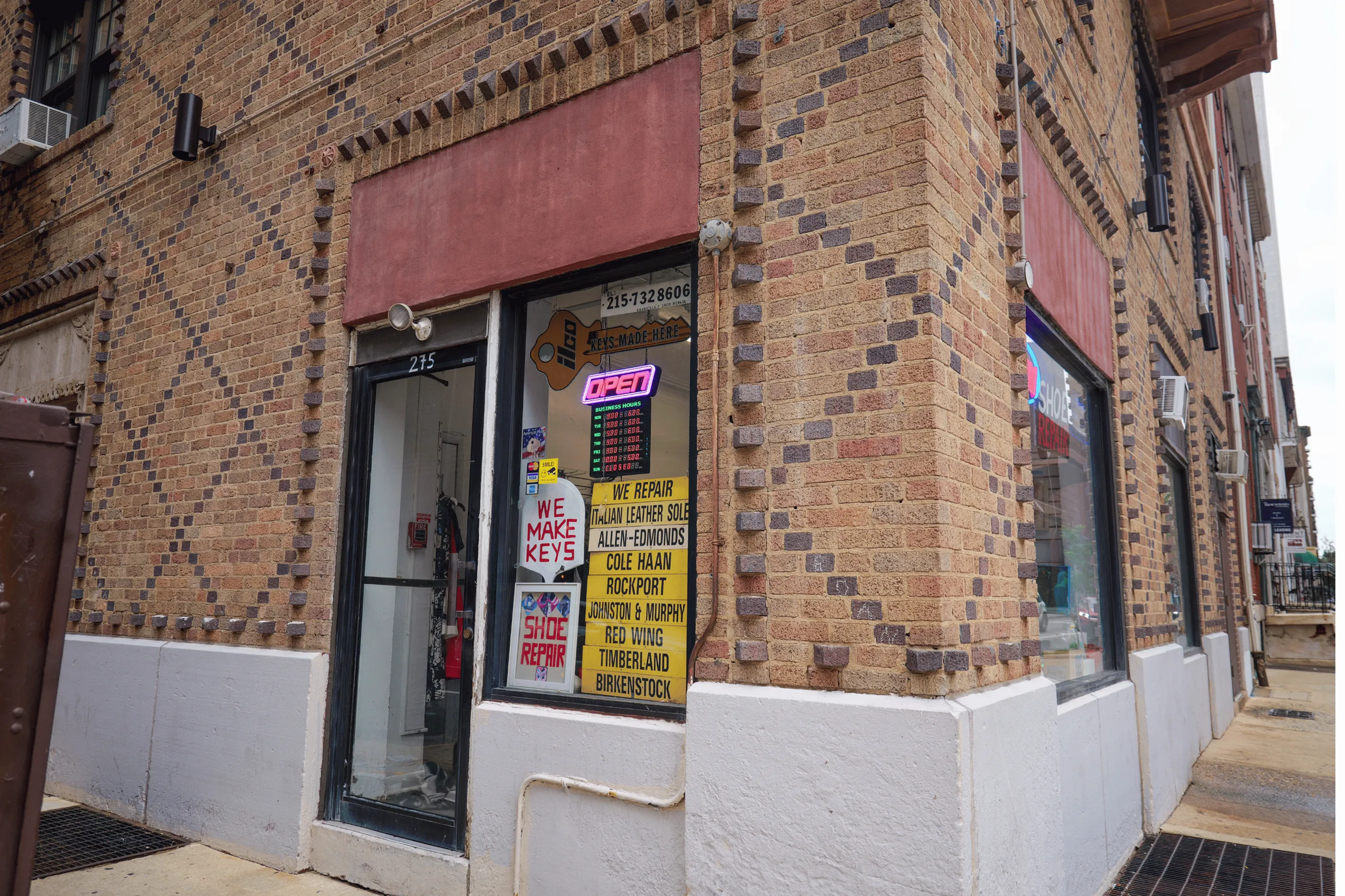 Charming brick storefront offering key making and shoe repair services, showcasing a vibrant open sign and detailed repair options in a welcoming urban setting.