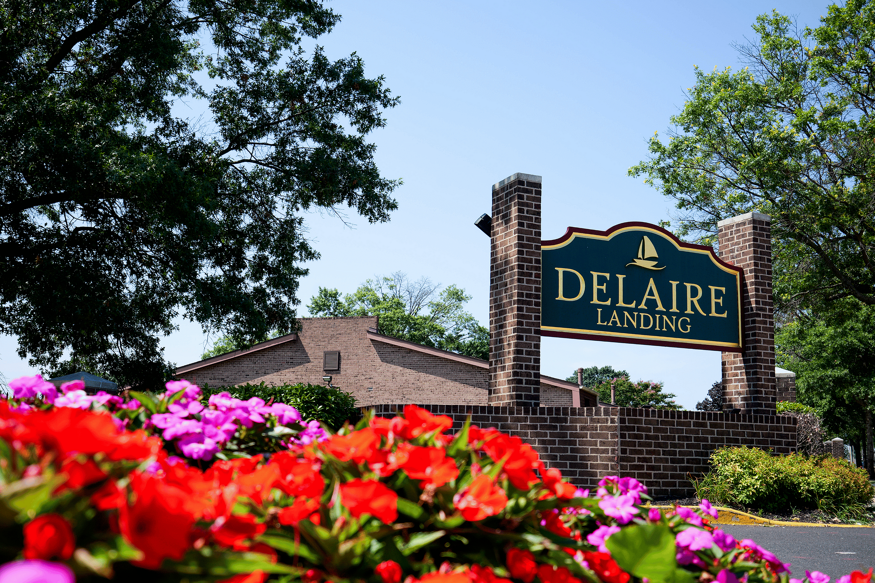 Charming entrance sign of Delaire Landing surrounded by vibrant red and pink flowers, set against a backdrop of lush greenery and a clear blue sky.