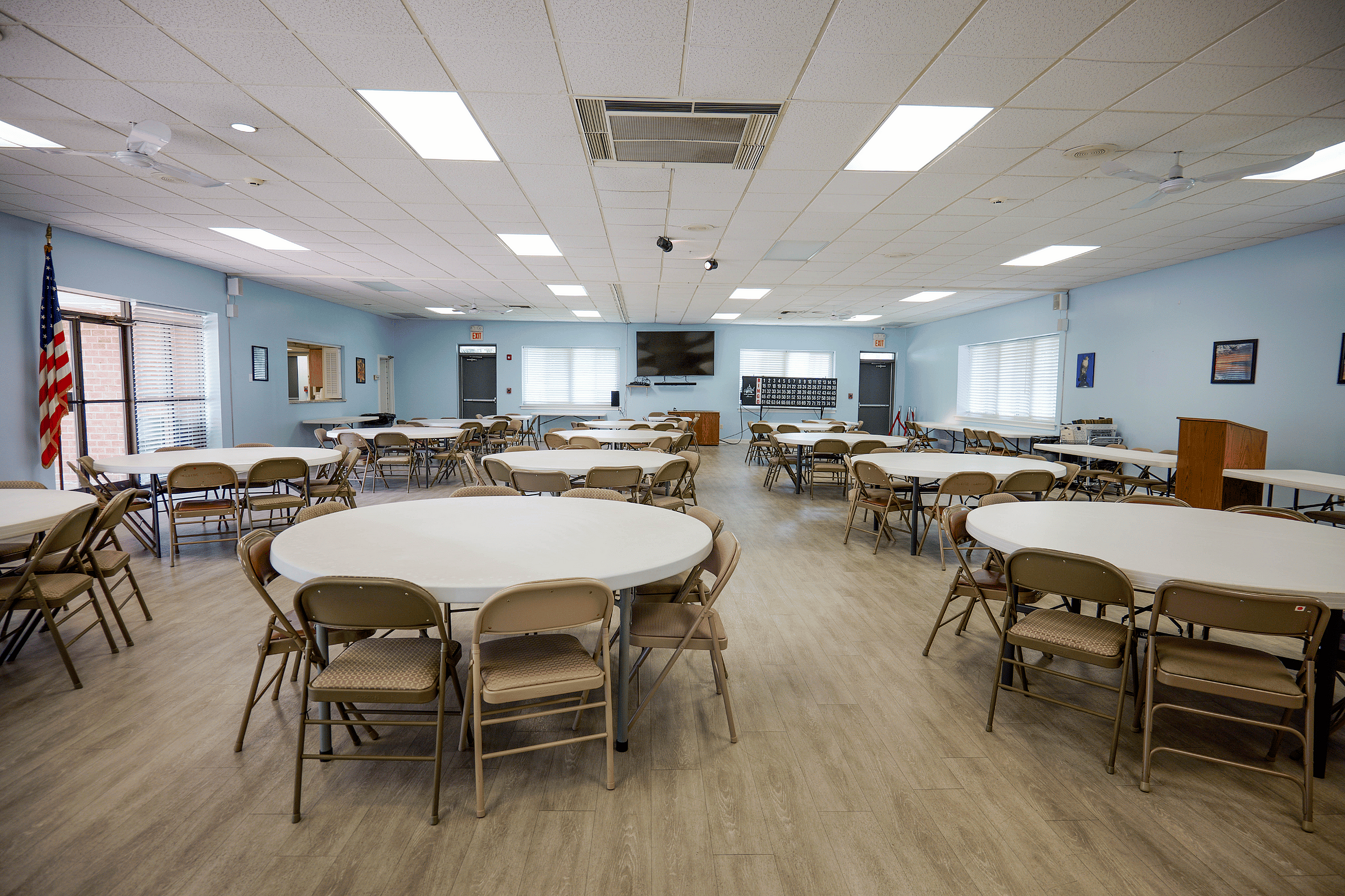 Spacious event room with round tables, elegant lighting, and warm wooden flooring, ideal for gatherings and meetings.