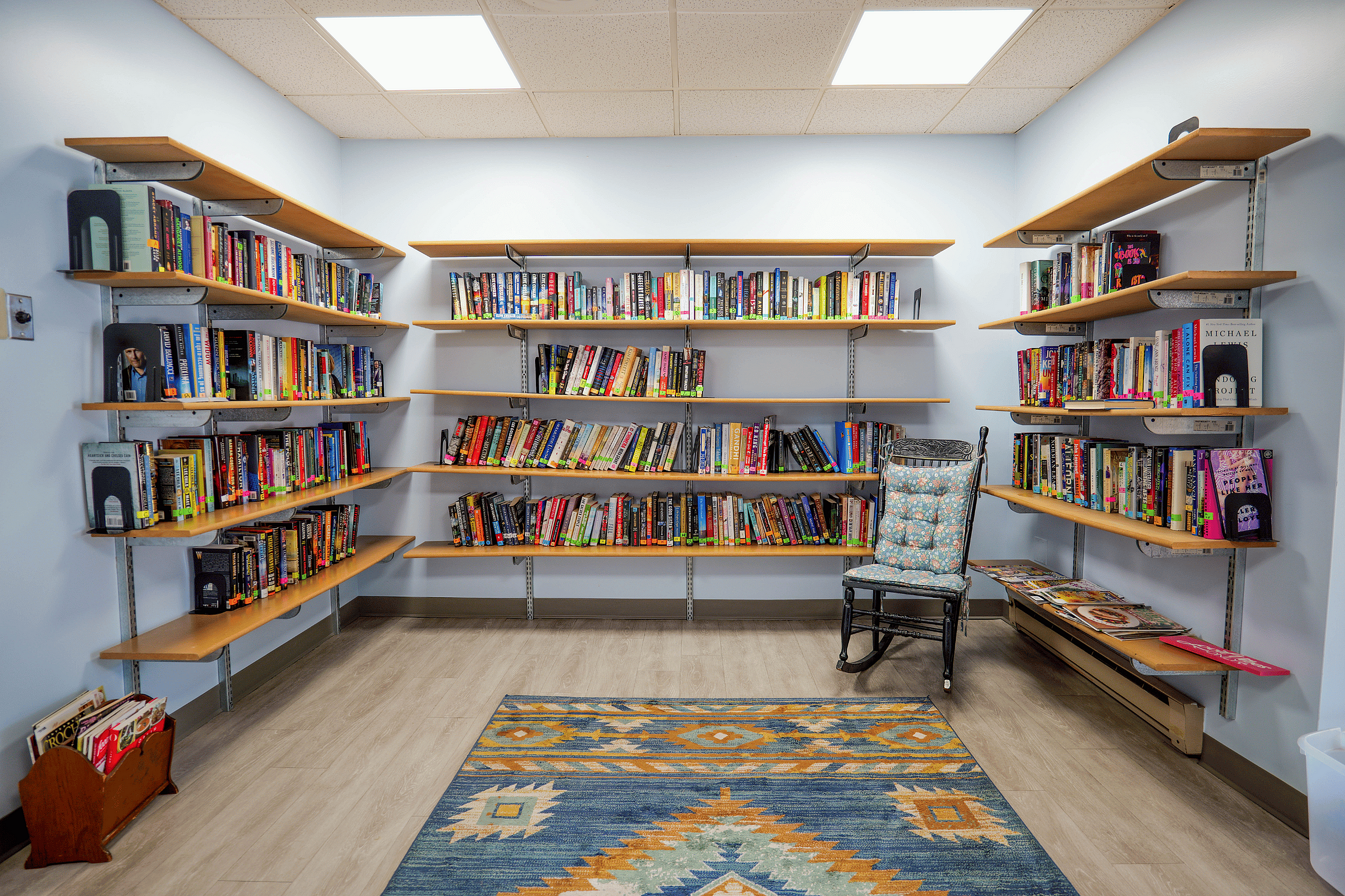 Charming and cozy reading nook featuring wall-mounted shelves filled with colorful books, a cushioned rocking chair, and a vibrant patterned rug.