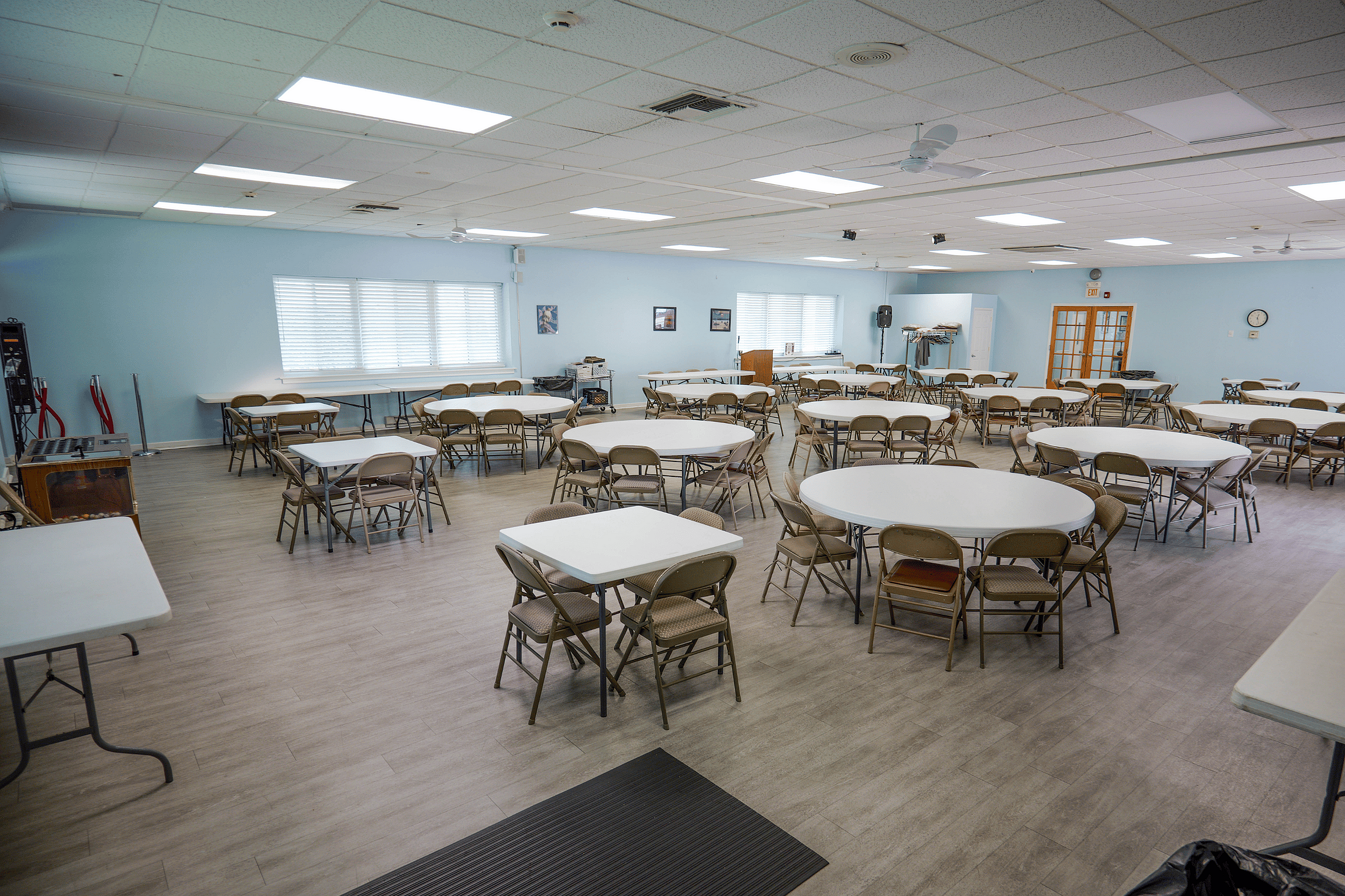 Spacious multi-purpose room with modern lighting, numerous tables and chairs, ideal for events and gatherings.