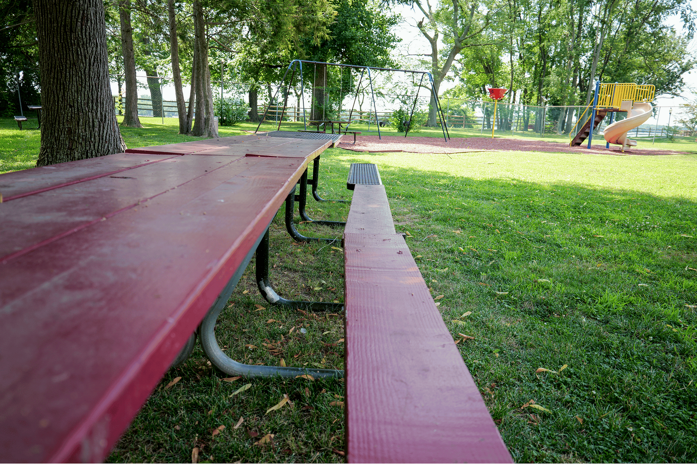 Charming park with vibrant playground, a long picnic table, and lush green surroundings perfect for outdoor relaxation and family fun.