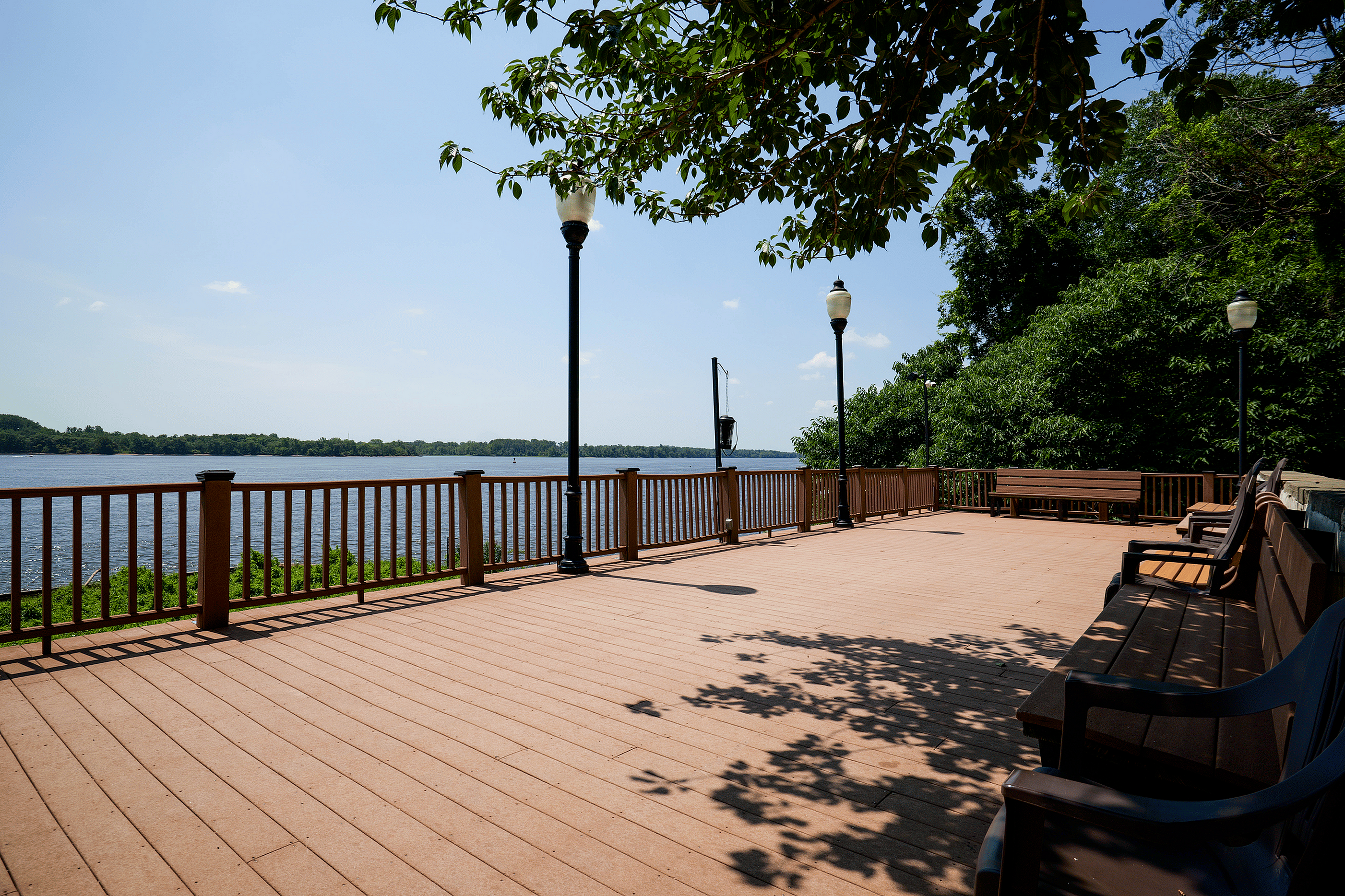 Scenic waterfront deck with inviting benches, surrounded by lush greenery and panoramic river views.