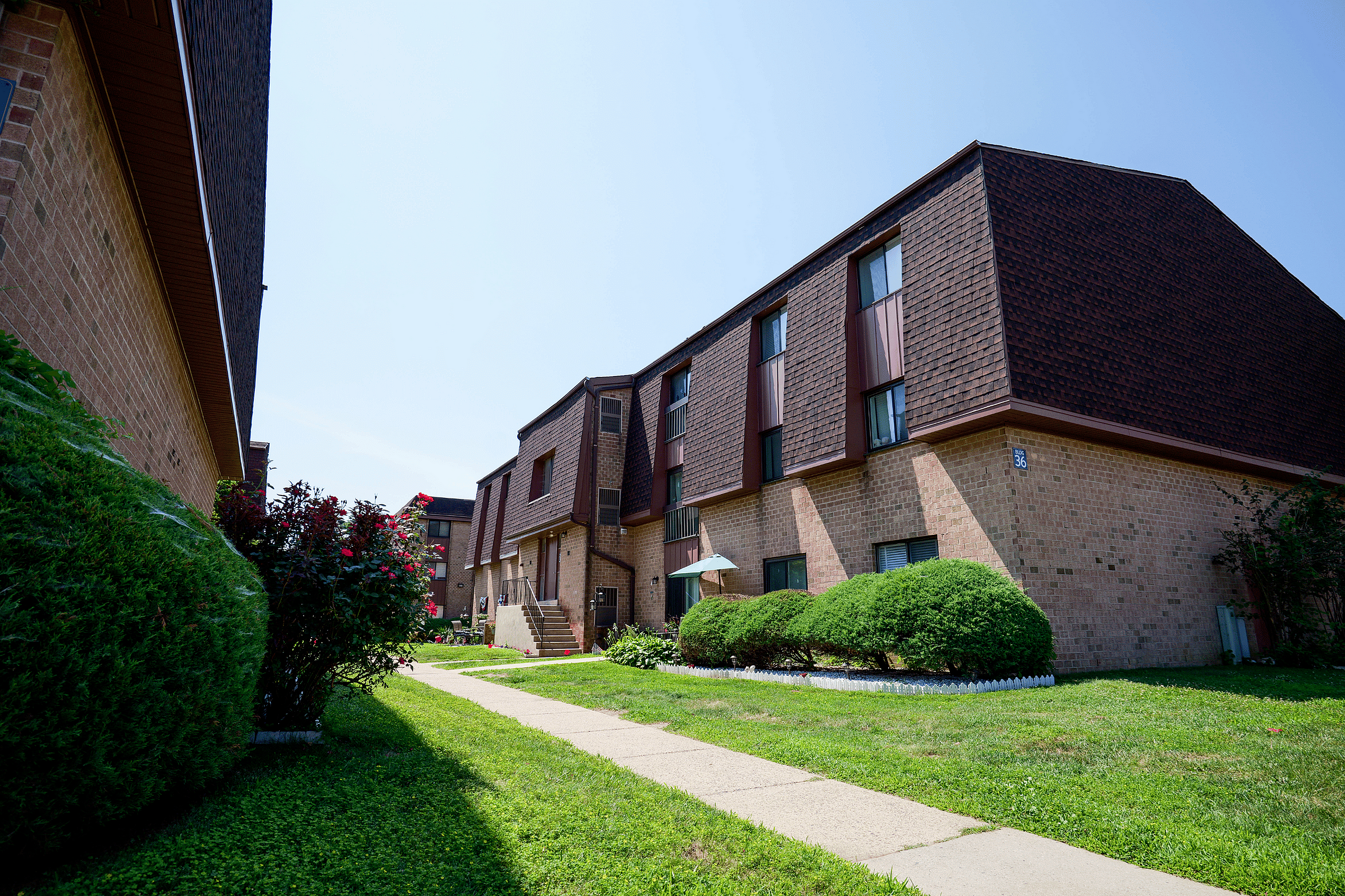 Charming brick apartment complex with lush greenery and a welcoming path, perfect for tranquil living.
