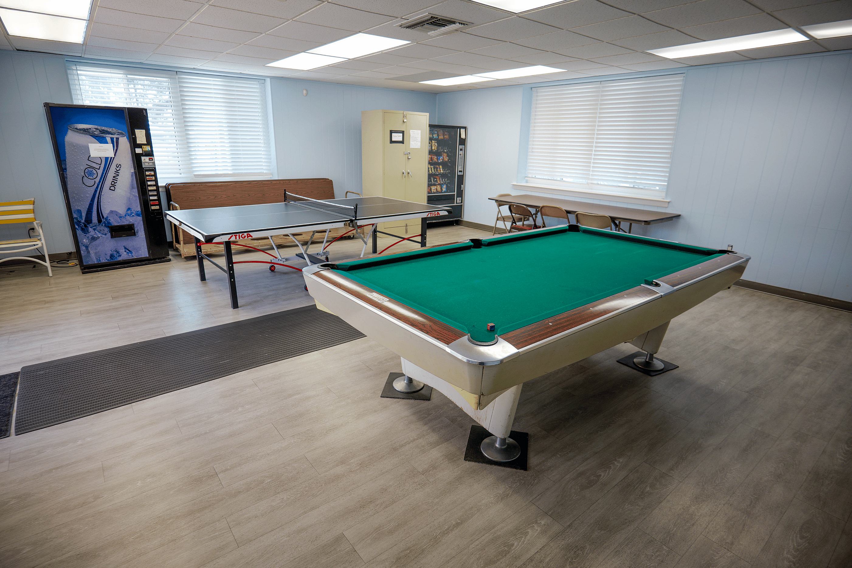 Bright recreational room with a pool table, ping pong table, and vending machines, perfect for social gatherings and entertainment.