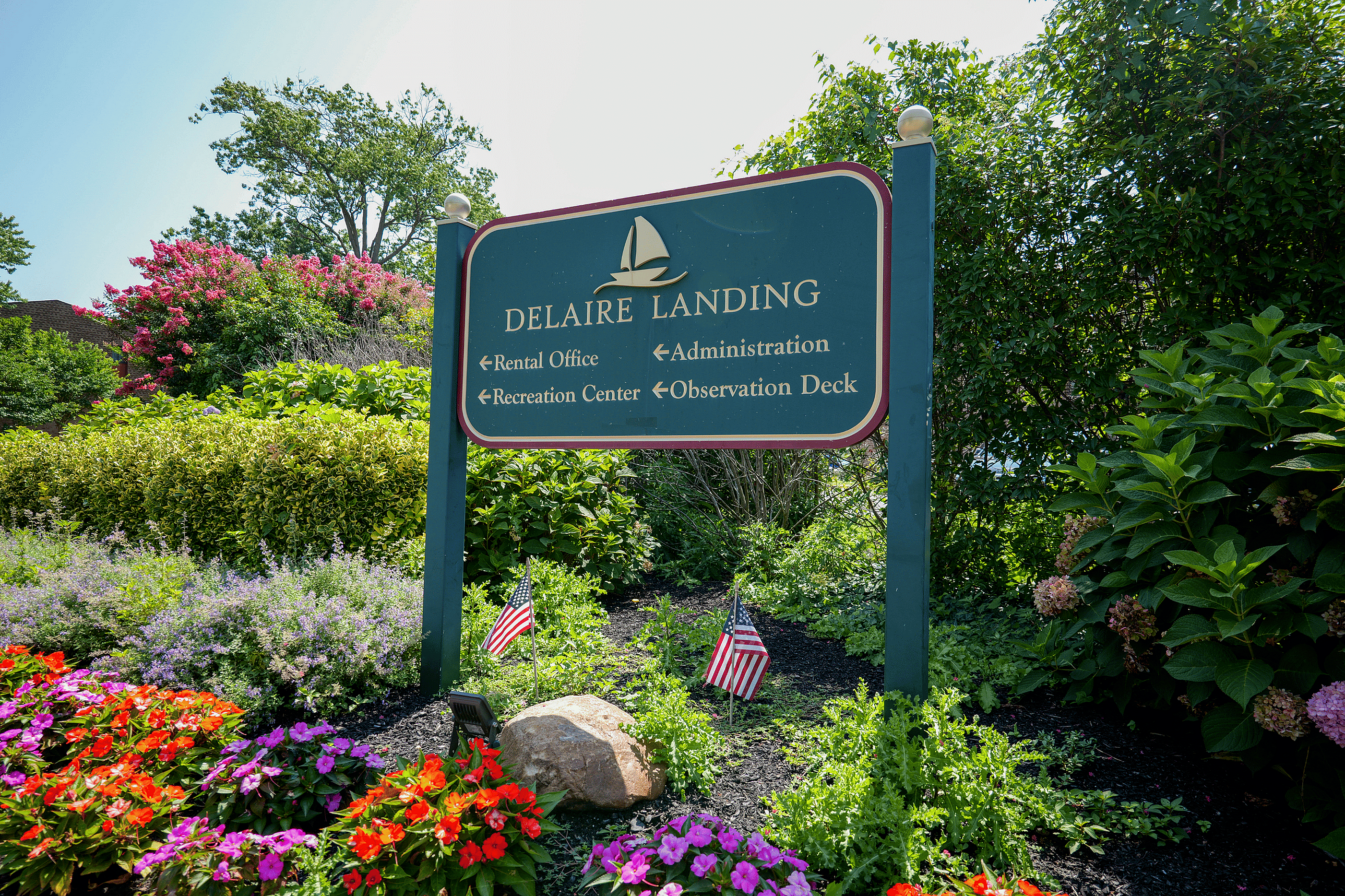 Charming entrance sign for Delaire Landing, surrounded by vibrant flowers and lush greenery, inviting visitors to explore the rental office, recreation center, and observation deck.