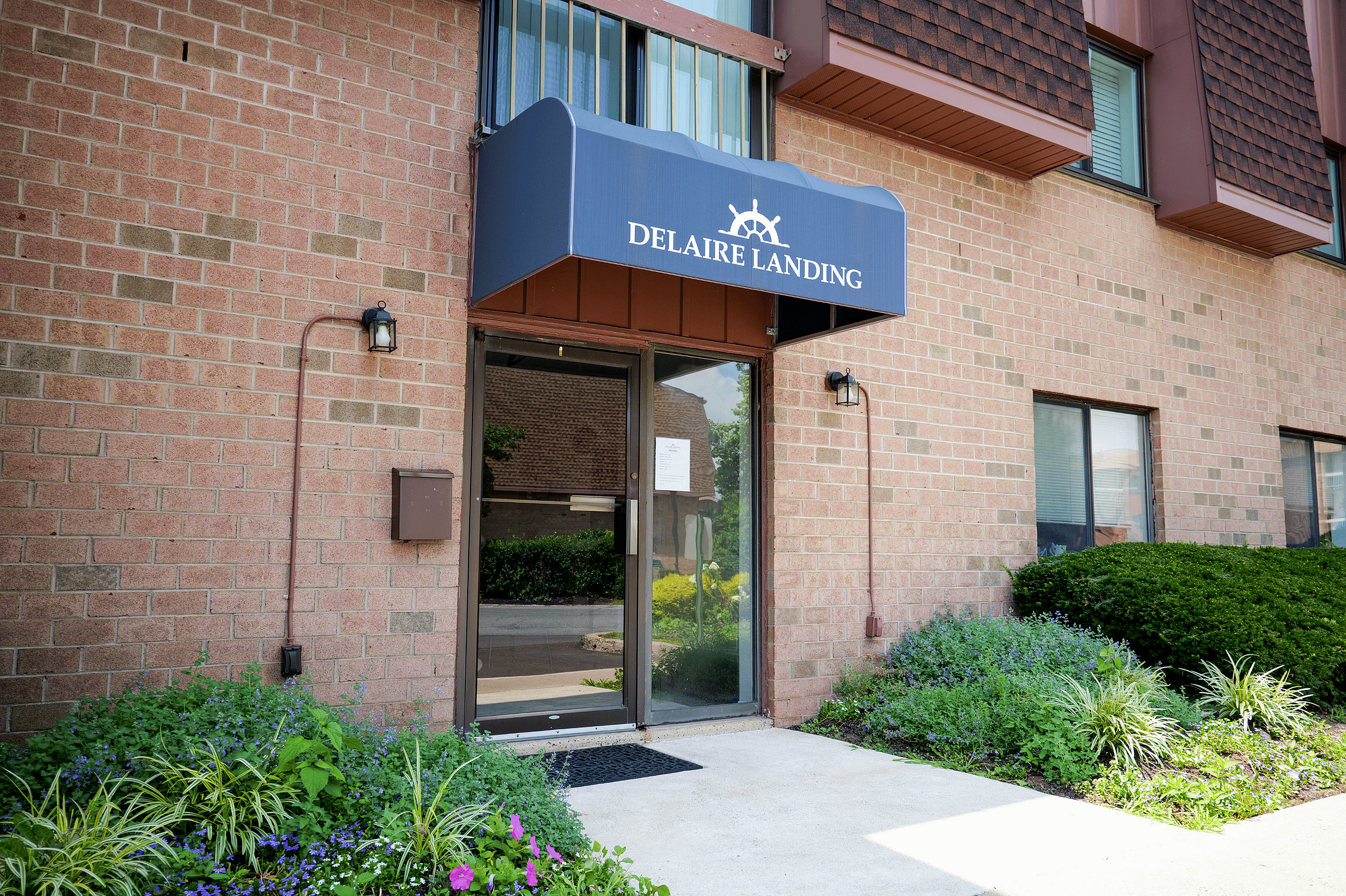 Inviting entrance of Delaire Landing, featuring a brick facade with lush landscaping and a charming awning.