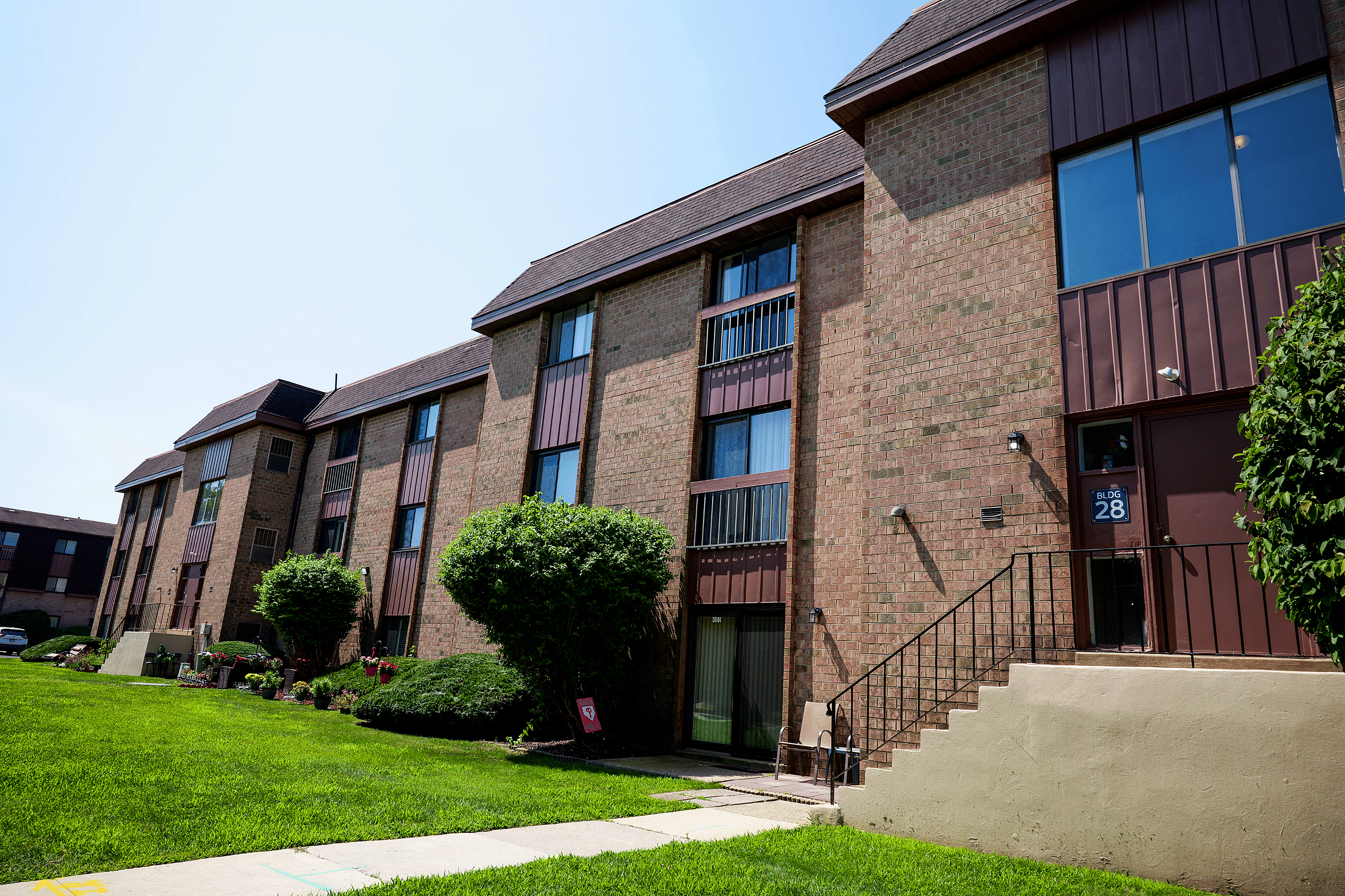 Charming brick apartment complex with lush green landscaping and inviting entrance in a peaceful neighborhood.